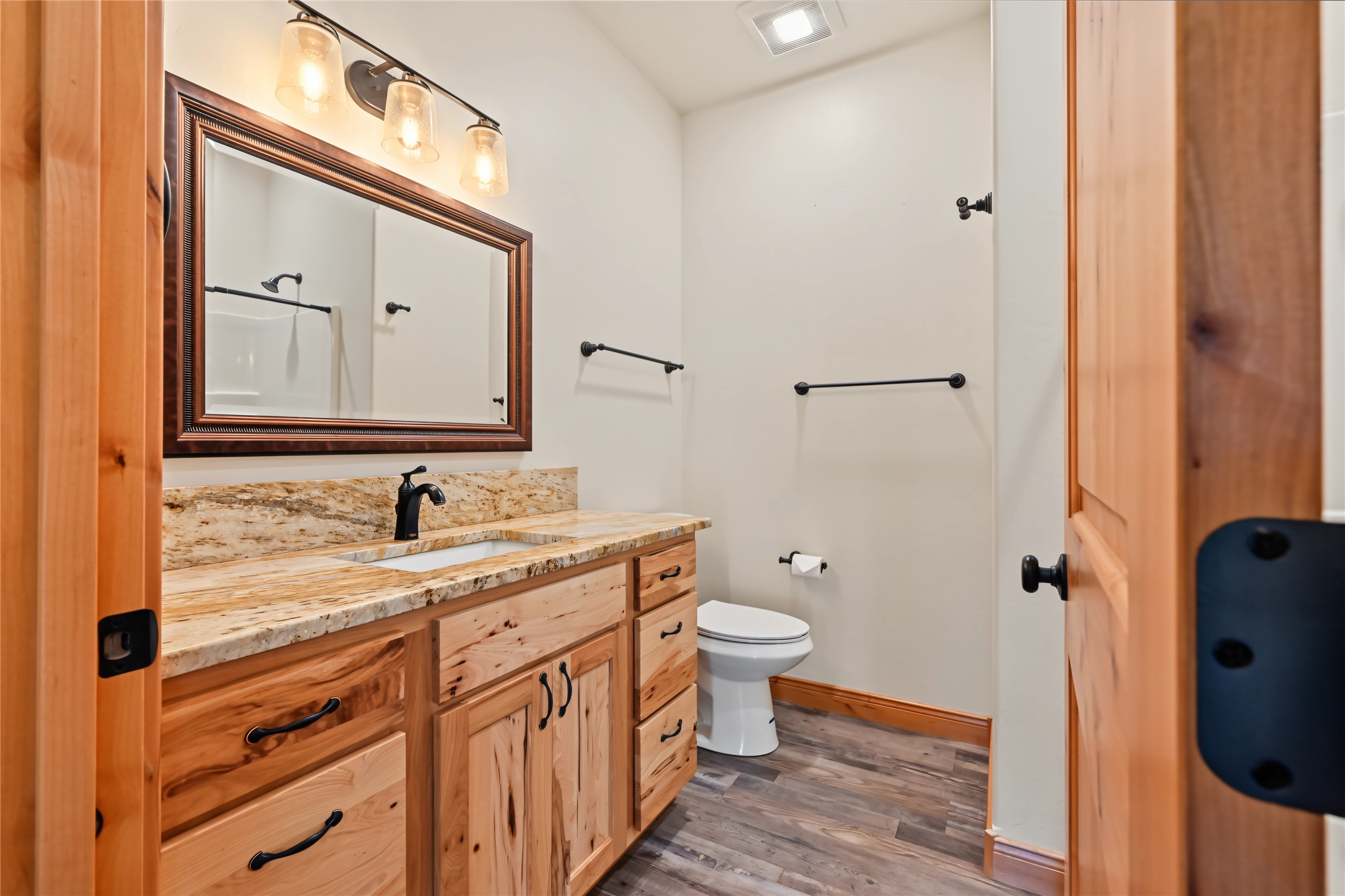 Bathroom with a natural wood vanity, stone countertop, framed mirror, and toilet.