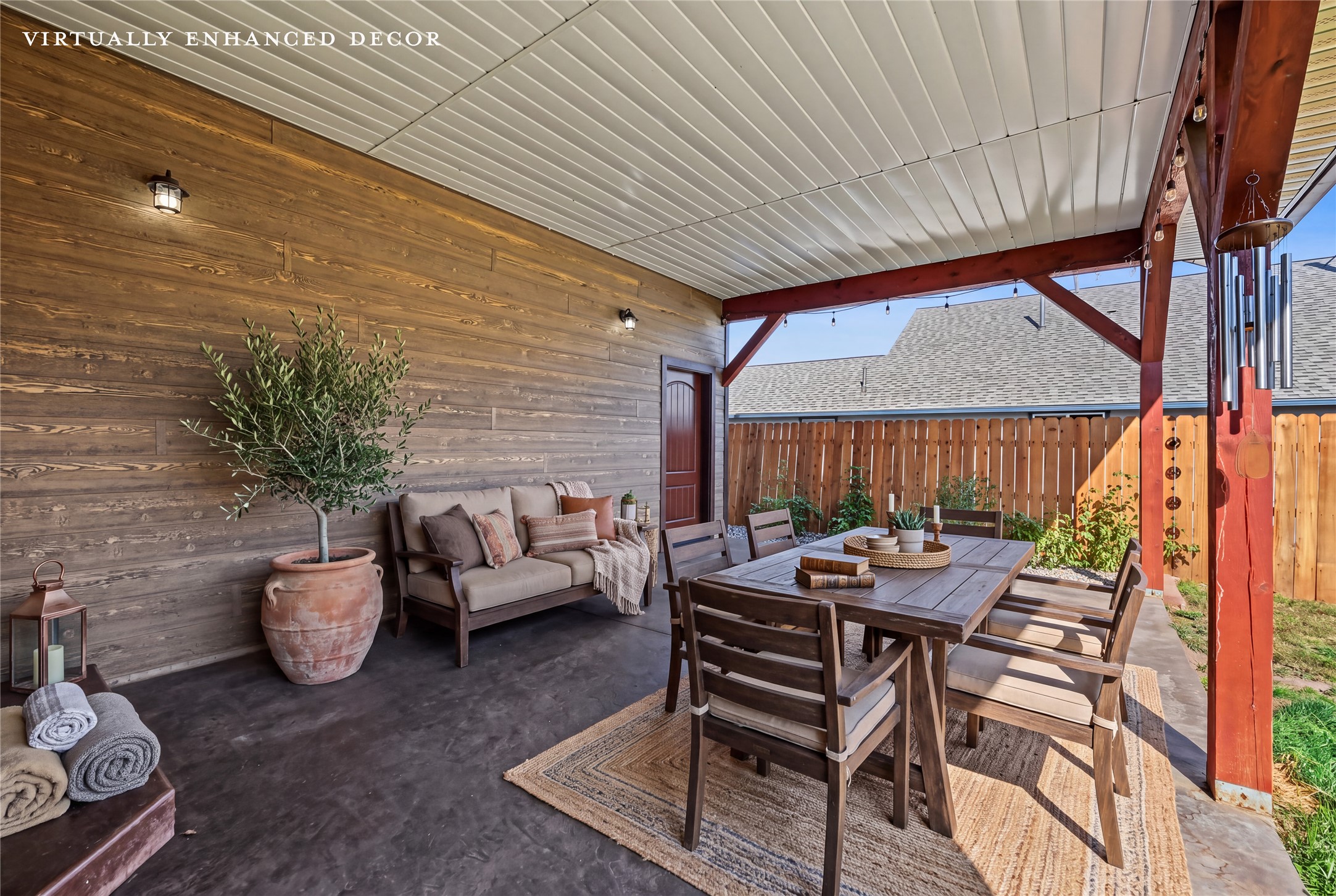 Covered patio with a wood dining set, cushioned sofa, potted tree, and exposed red beams.