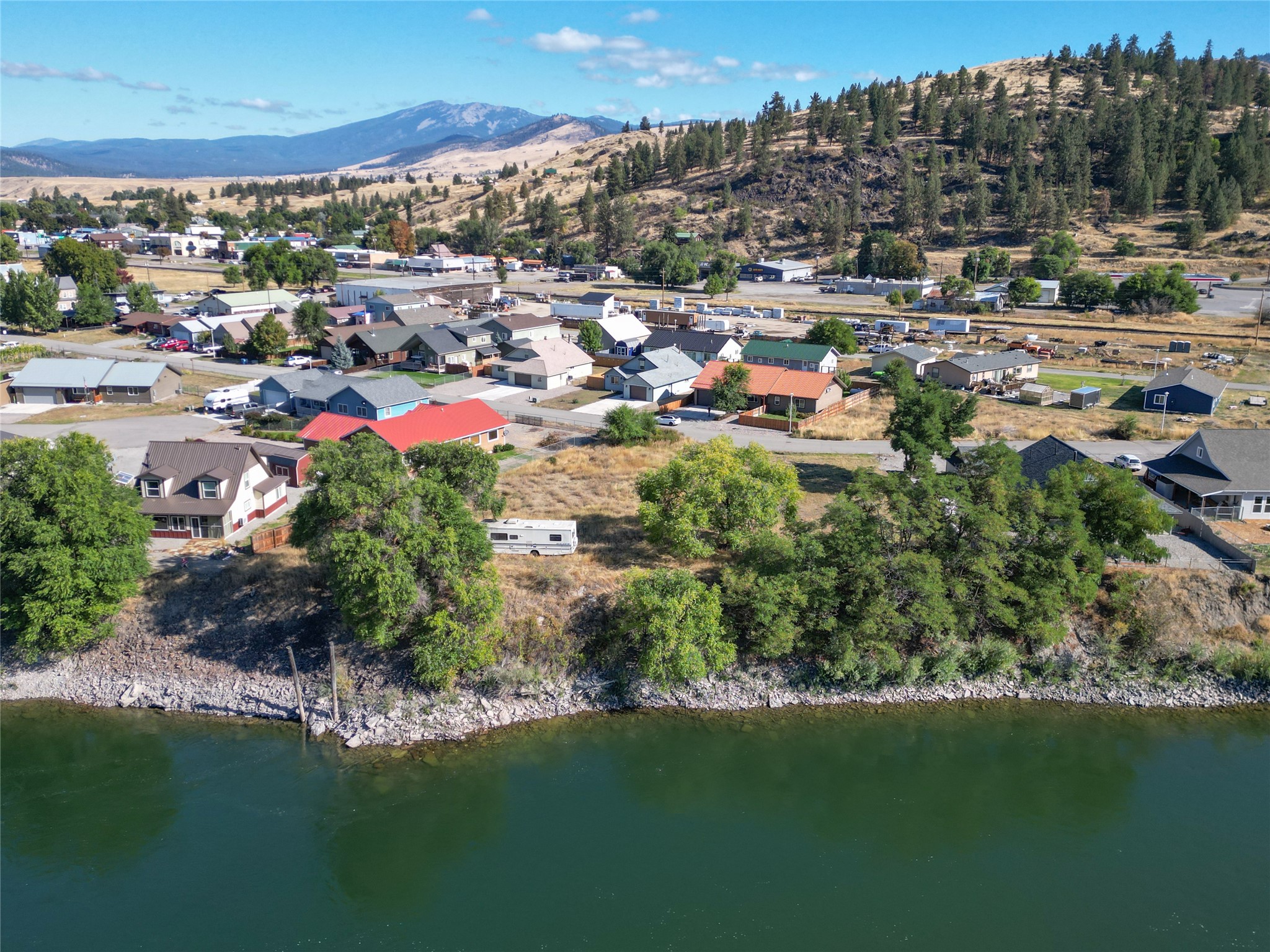 Aerial view of a riverside neighborhood, with the river in front and wooded hills and mountains beyond.