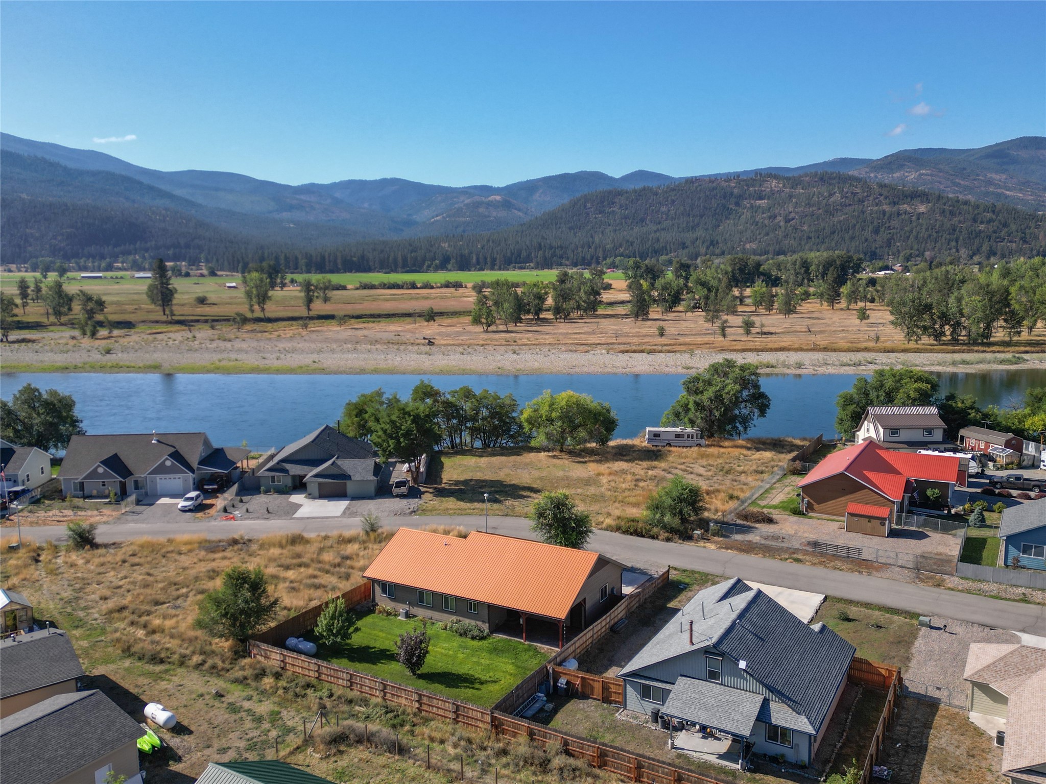 Aerial view of an orange-roofed house beside a river, with mountains beyond the surrounding neighborhood.