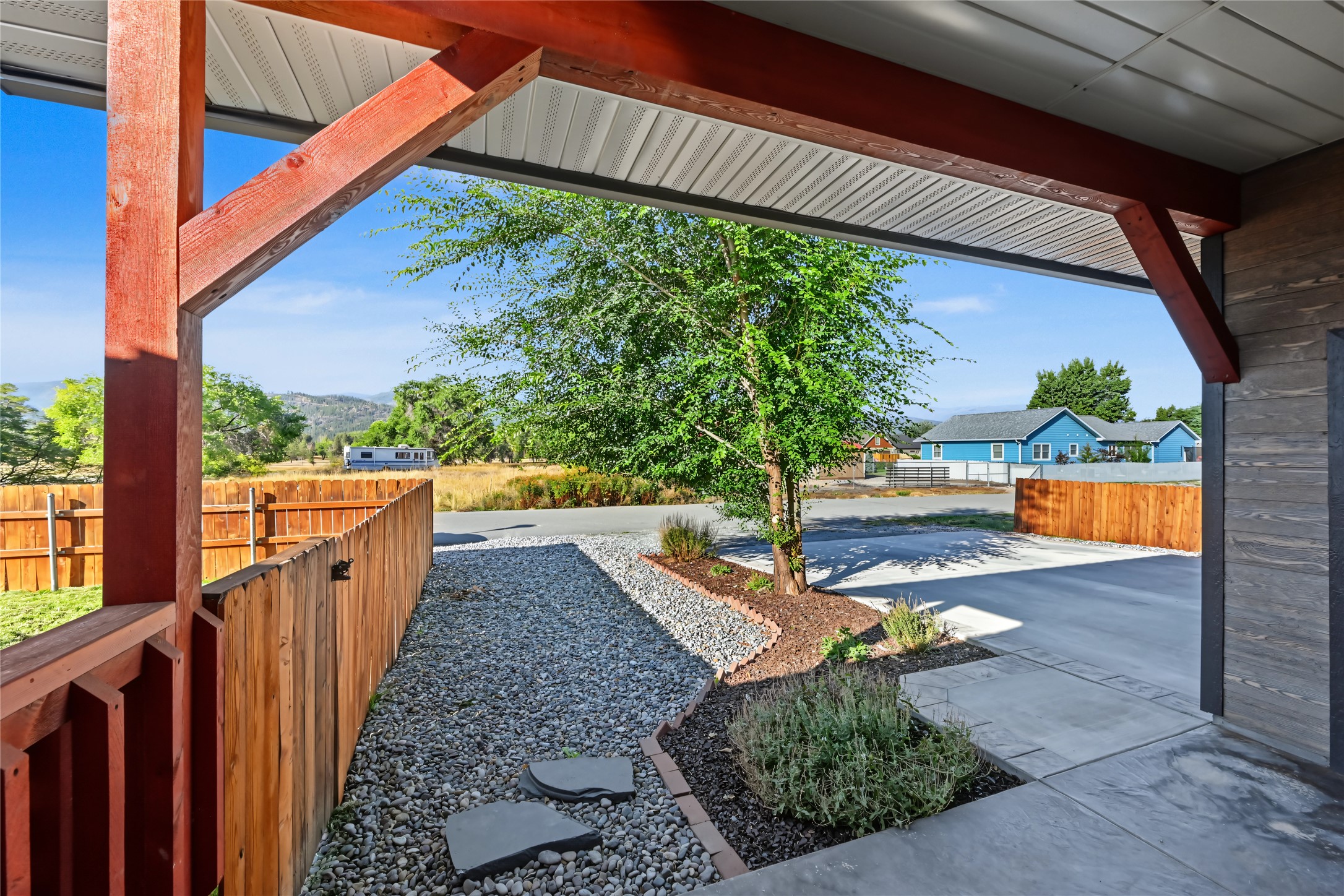 Covered patio with red timber beams, a gravel path, and landscaped planting beds.