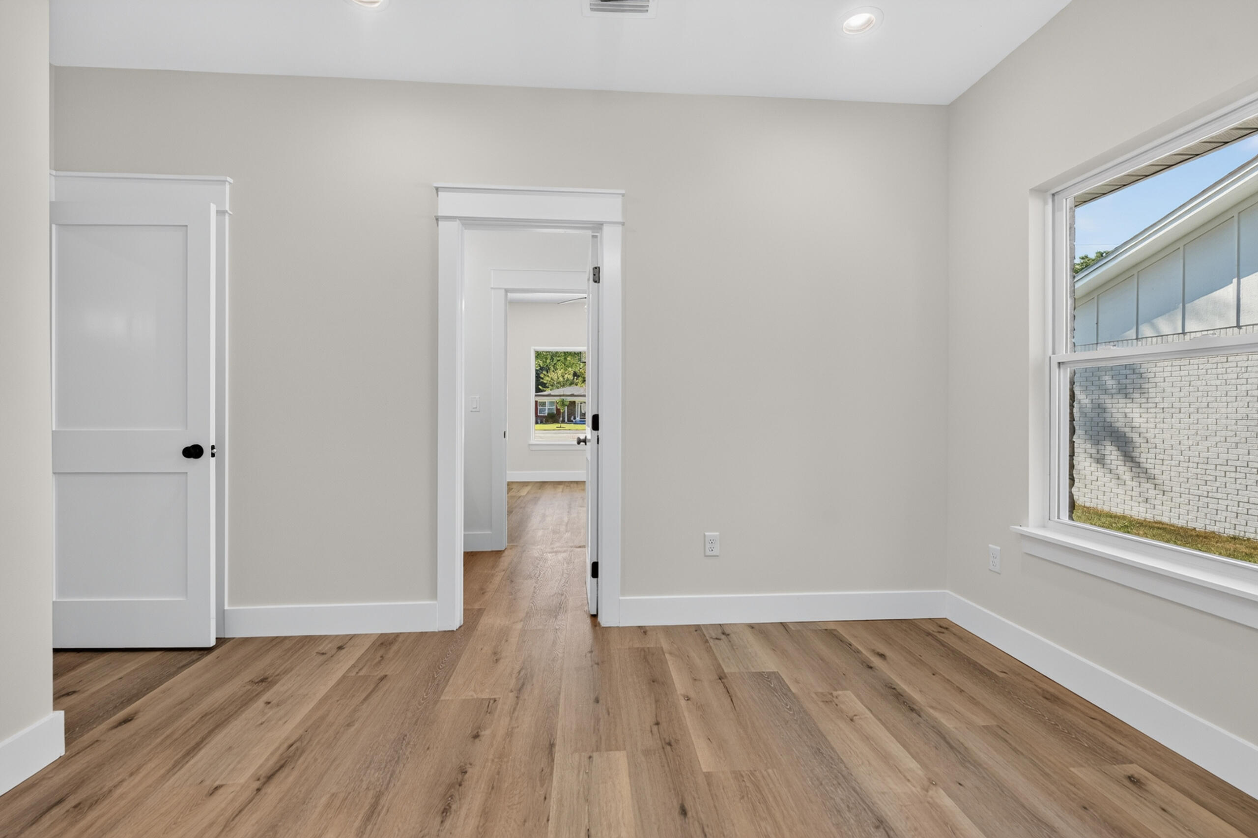 Empty room with wide-plank wood floors, white-trimmed doorways, and a large window.