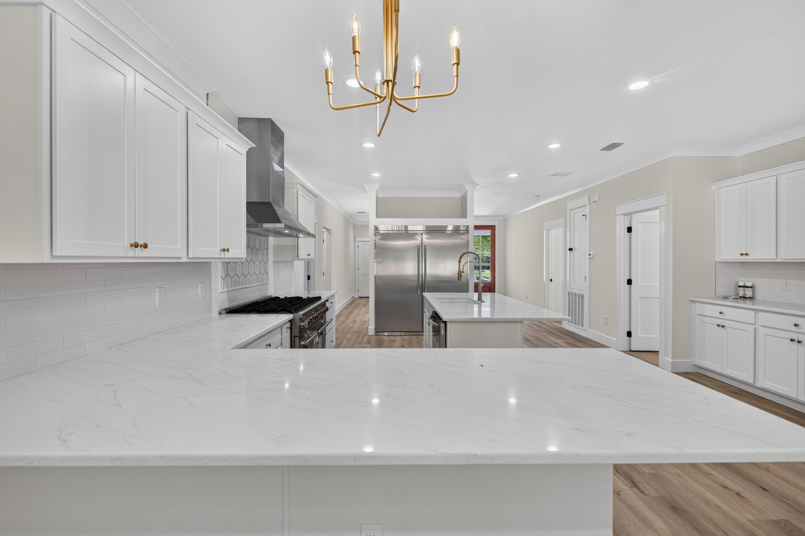 Kitchen with a broad white island, stainless steel appliances, and a gold chandelier.