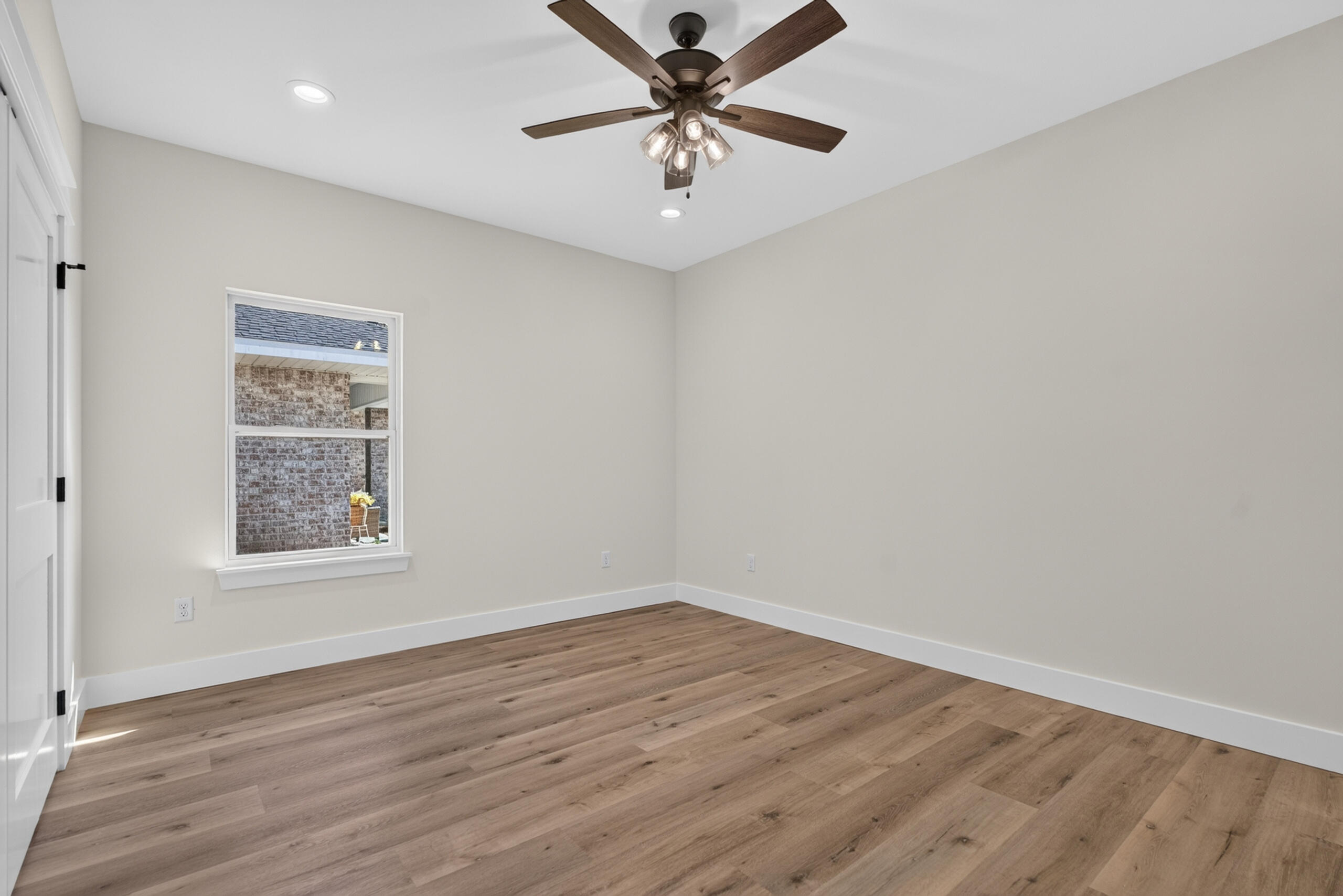Empty bedroom with wood plank flooring, a window, and a dark wood ceiling fan.