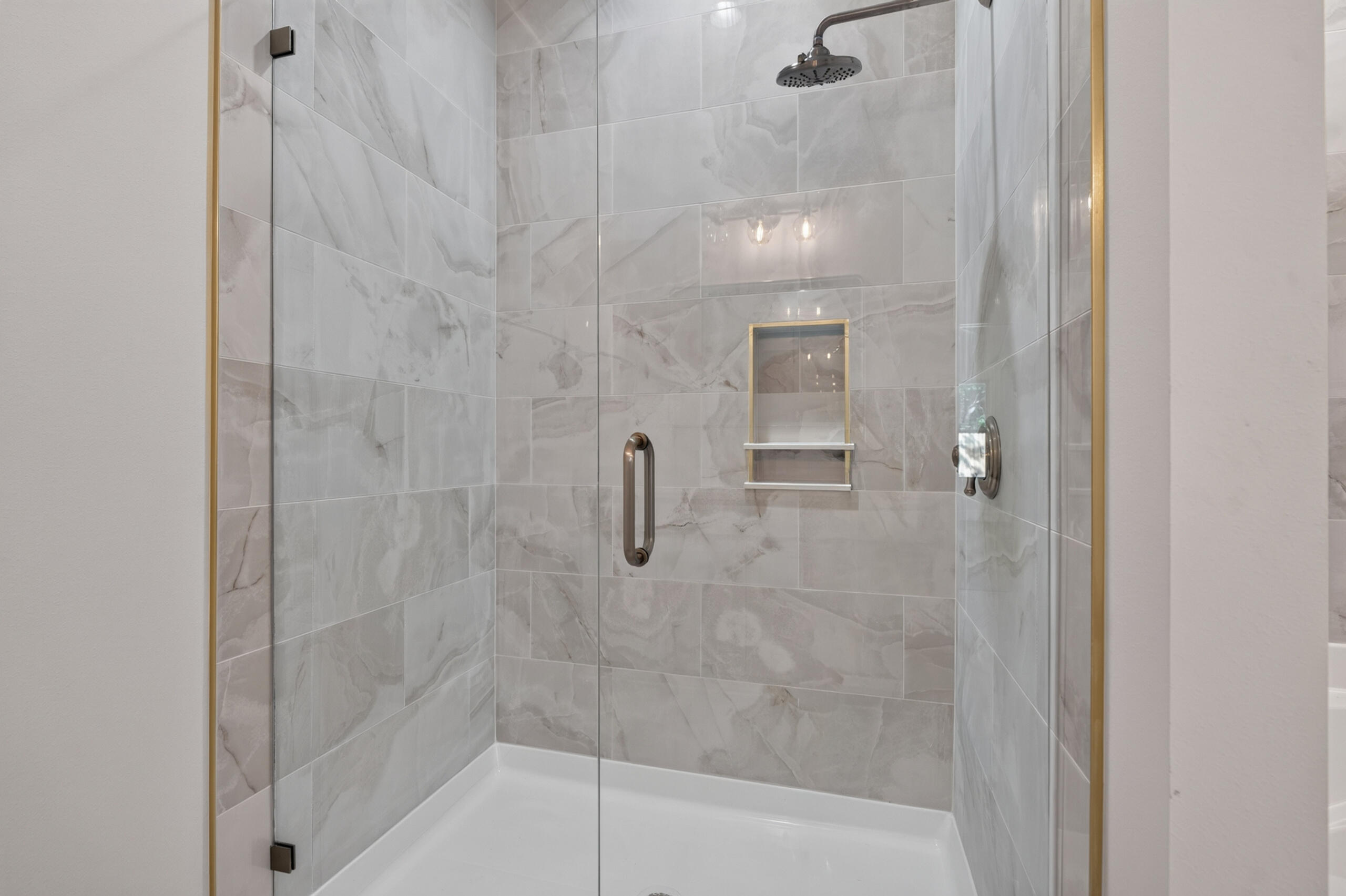 Walk-in shower with gray marble-look tile, glass panels, brass-toned trim, and a recessed niche.