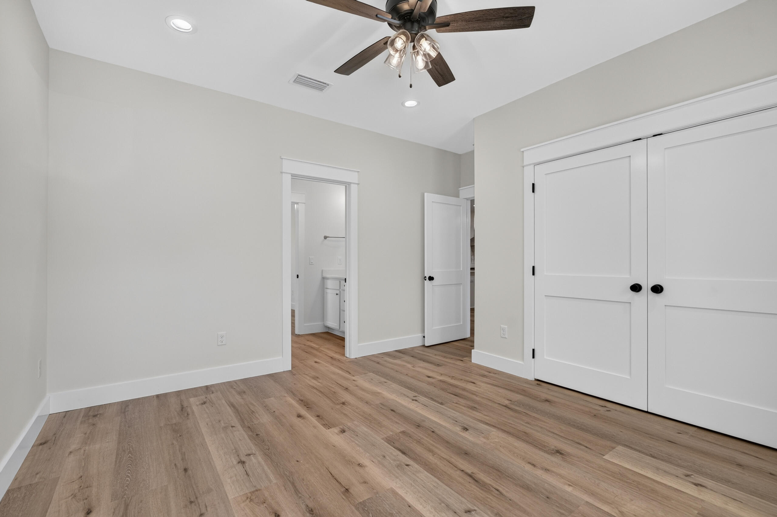Empty bedroom with wood-look flooring, double closet doors, and a ceiling fan.