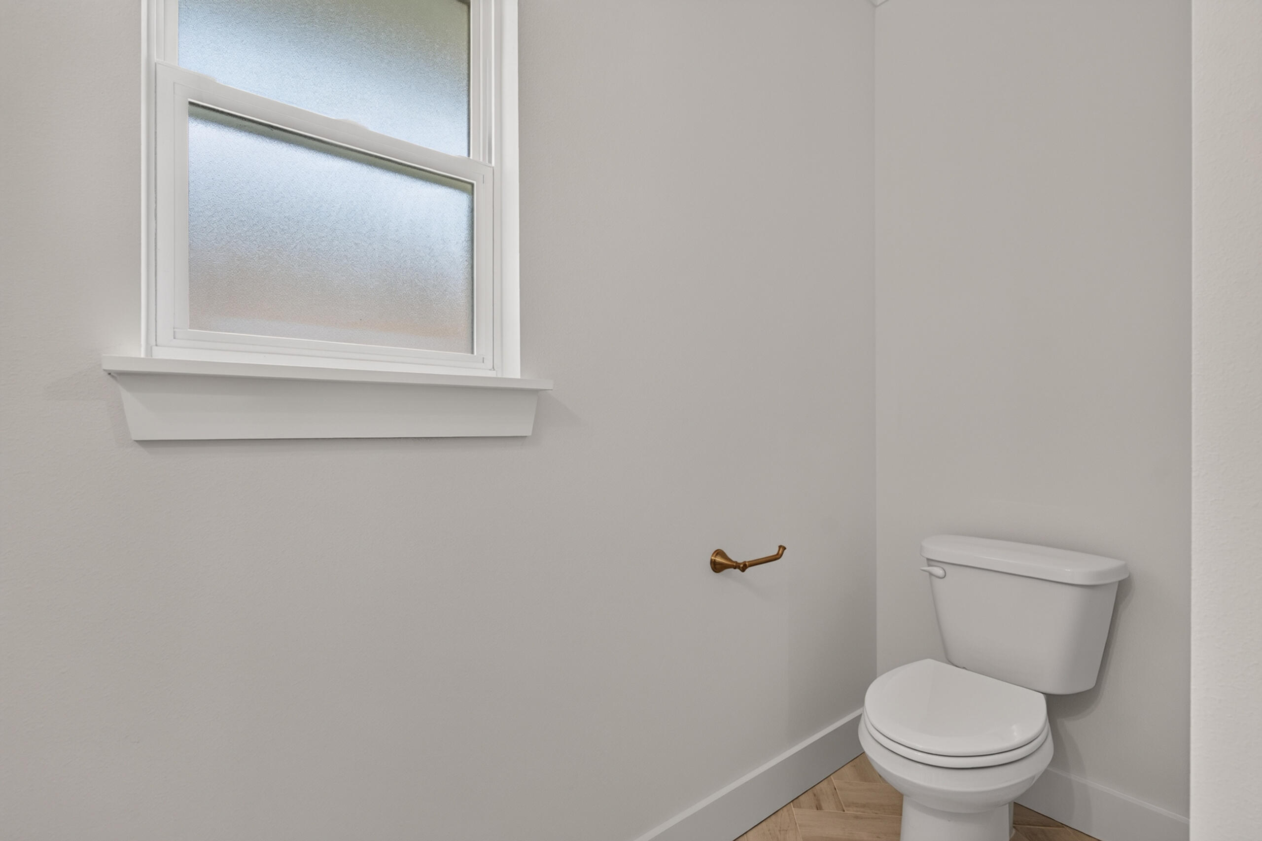 Bathroom with a white toilet beneath a frosted window and a brass toilet-paper holder.