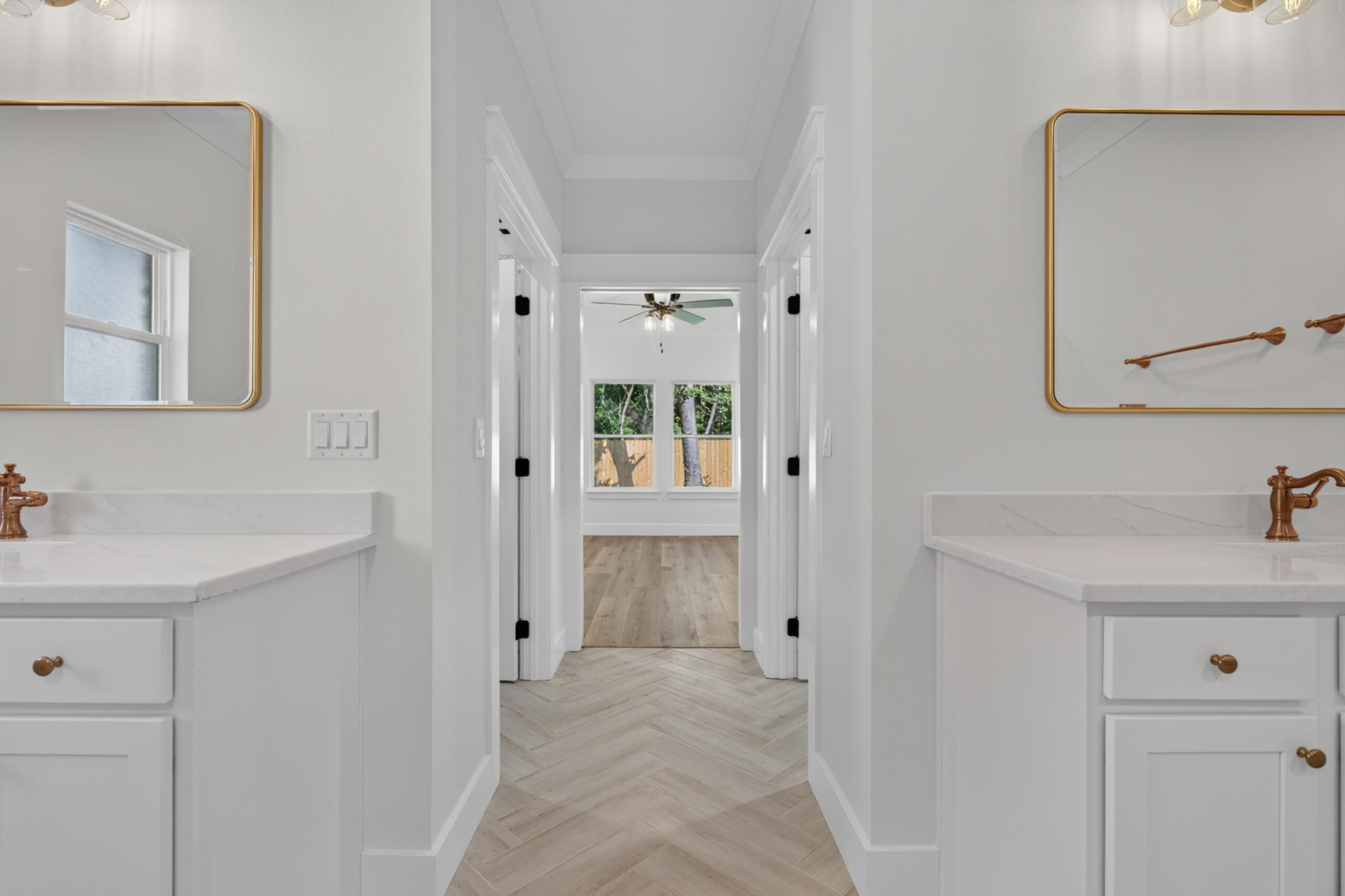 Bathroom with white double vanities and copper fixtures framing a view through to a wood-floored room.