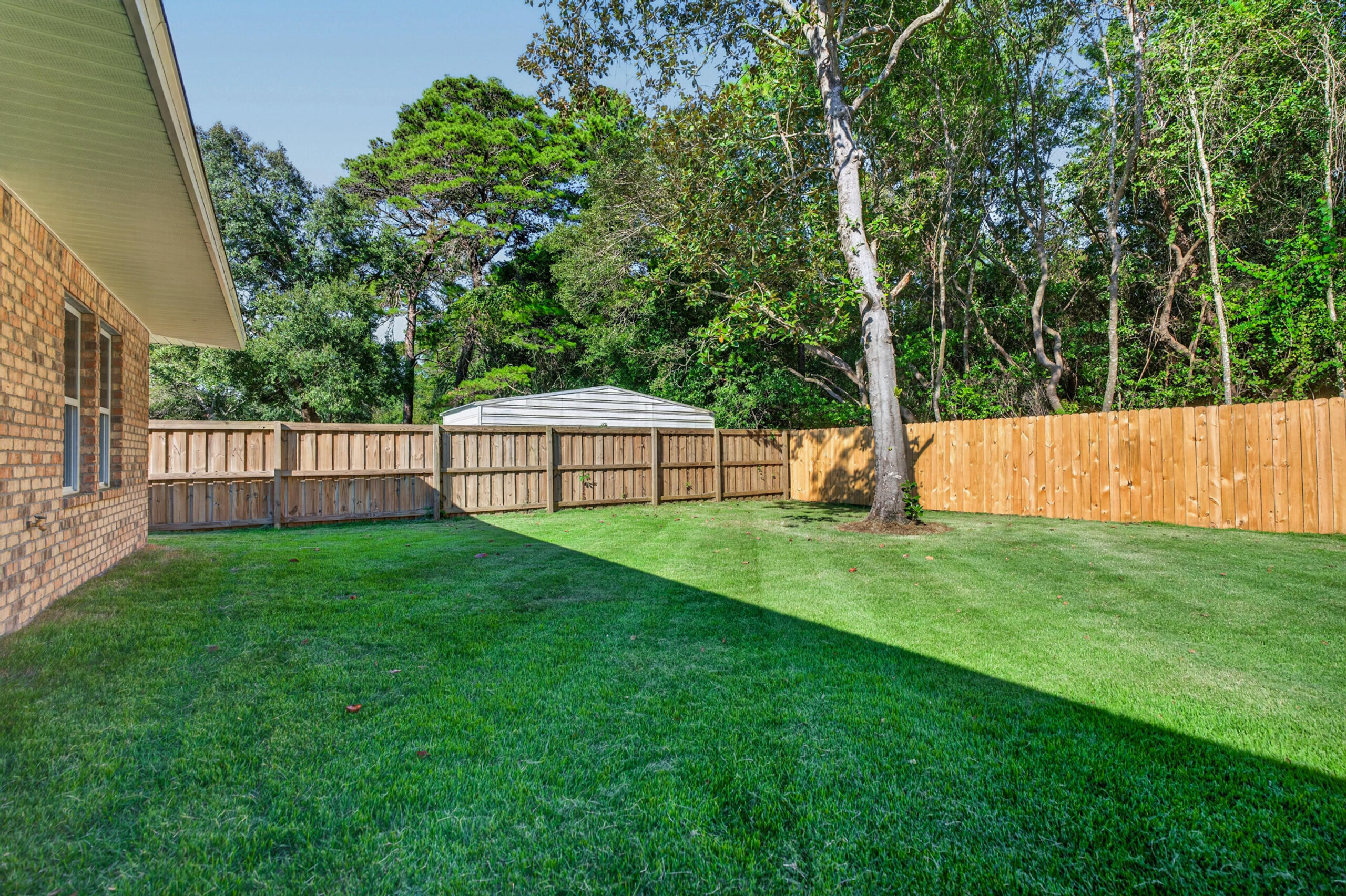 Fenced backyard with a broad lawn, mature trees, and a small shed behind the wooden fence.