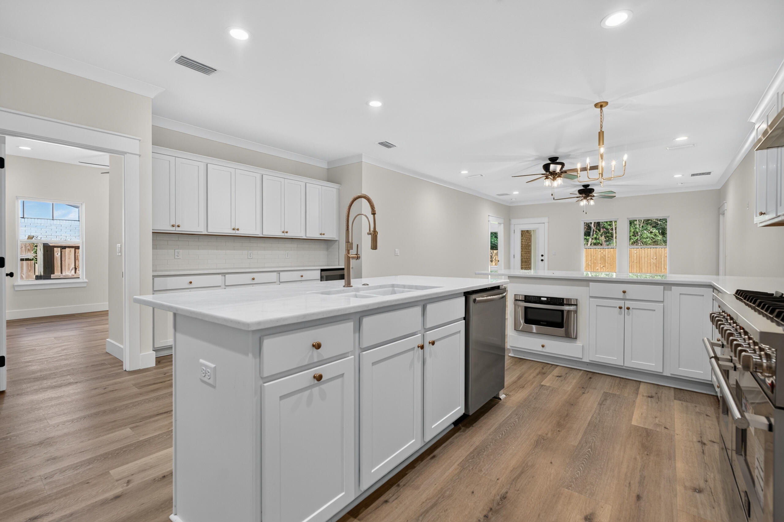 Kitchen with a large white island, brass faucet, stainless steel appliances, and wood-look floors.