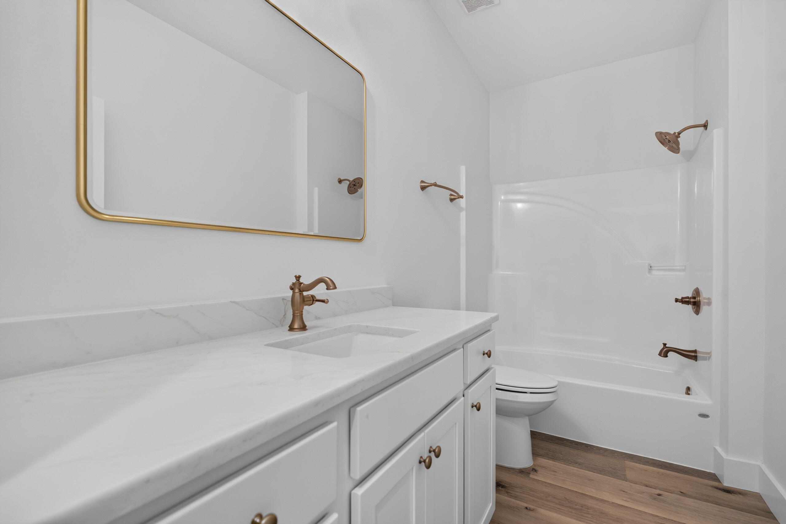 Bathroom with a white vanity, gold-framed mirror, bronze fixtures, and tub-shower.