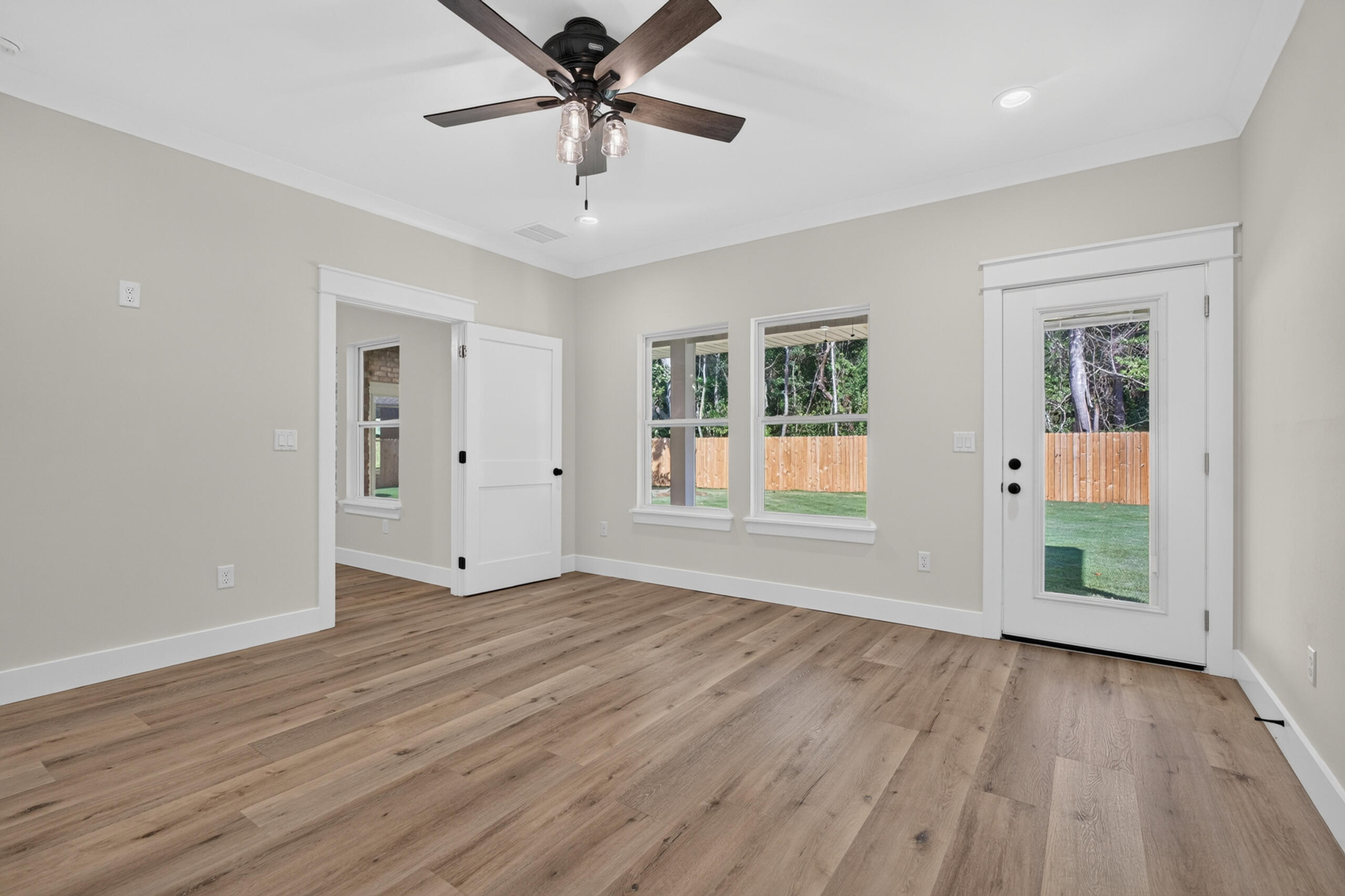 Unfurnished room with wood flooring, a ceiling fan, and a glass-panel door to the backyard.