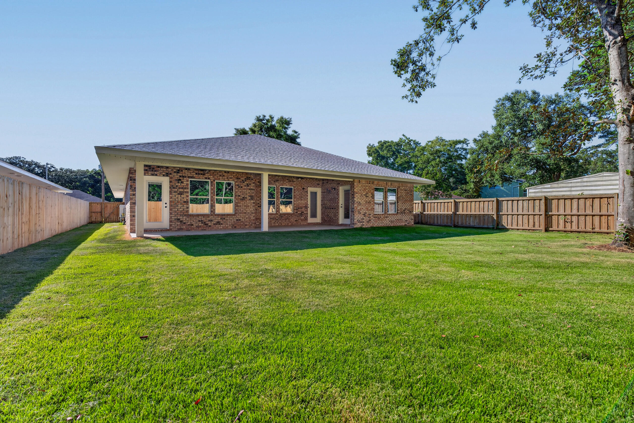 Brick home's rear exterior with a covered patio and spacious fenced lawn.