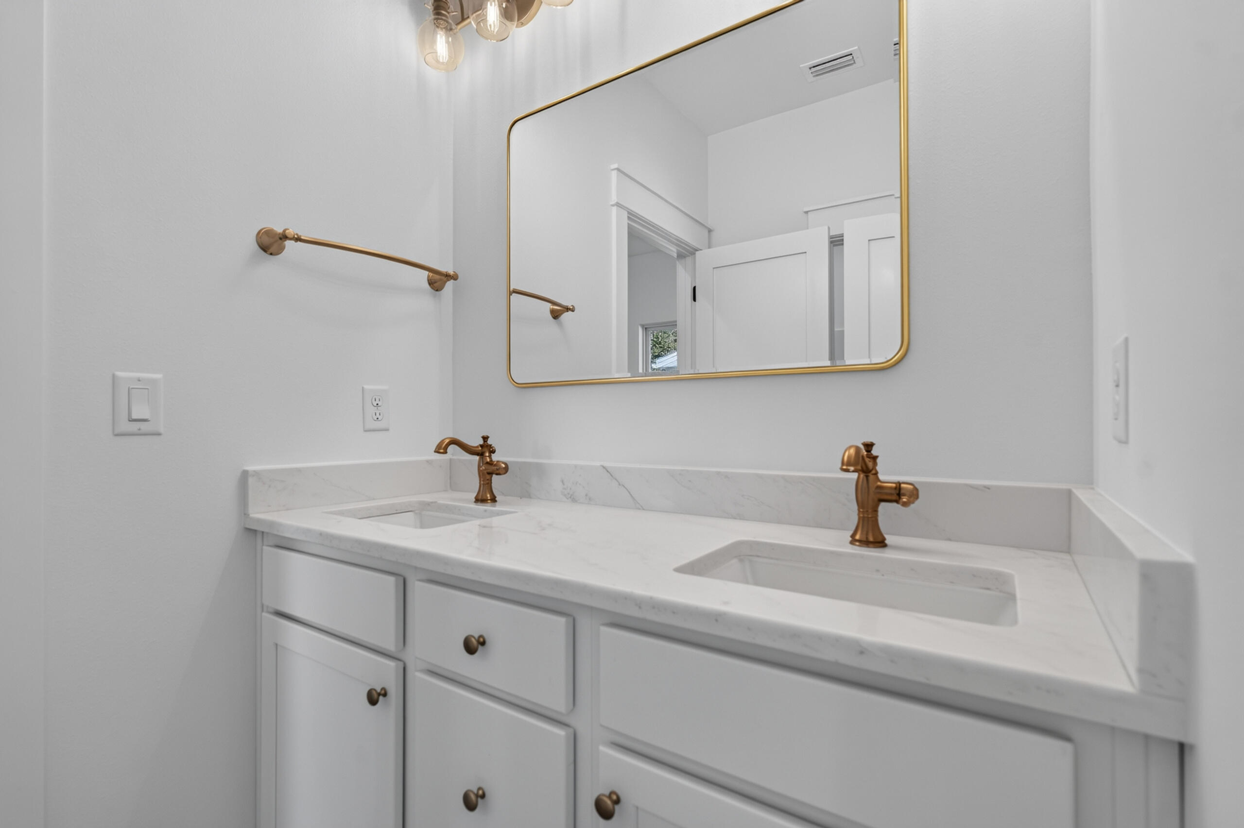 Bathroom double vanity with a marble-look counter, brass faucets, and gold-framed mirror.