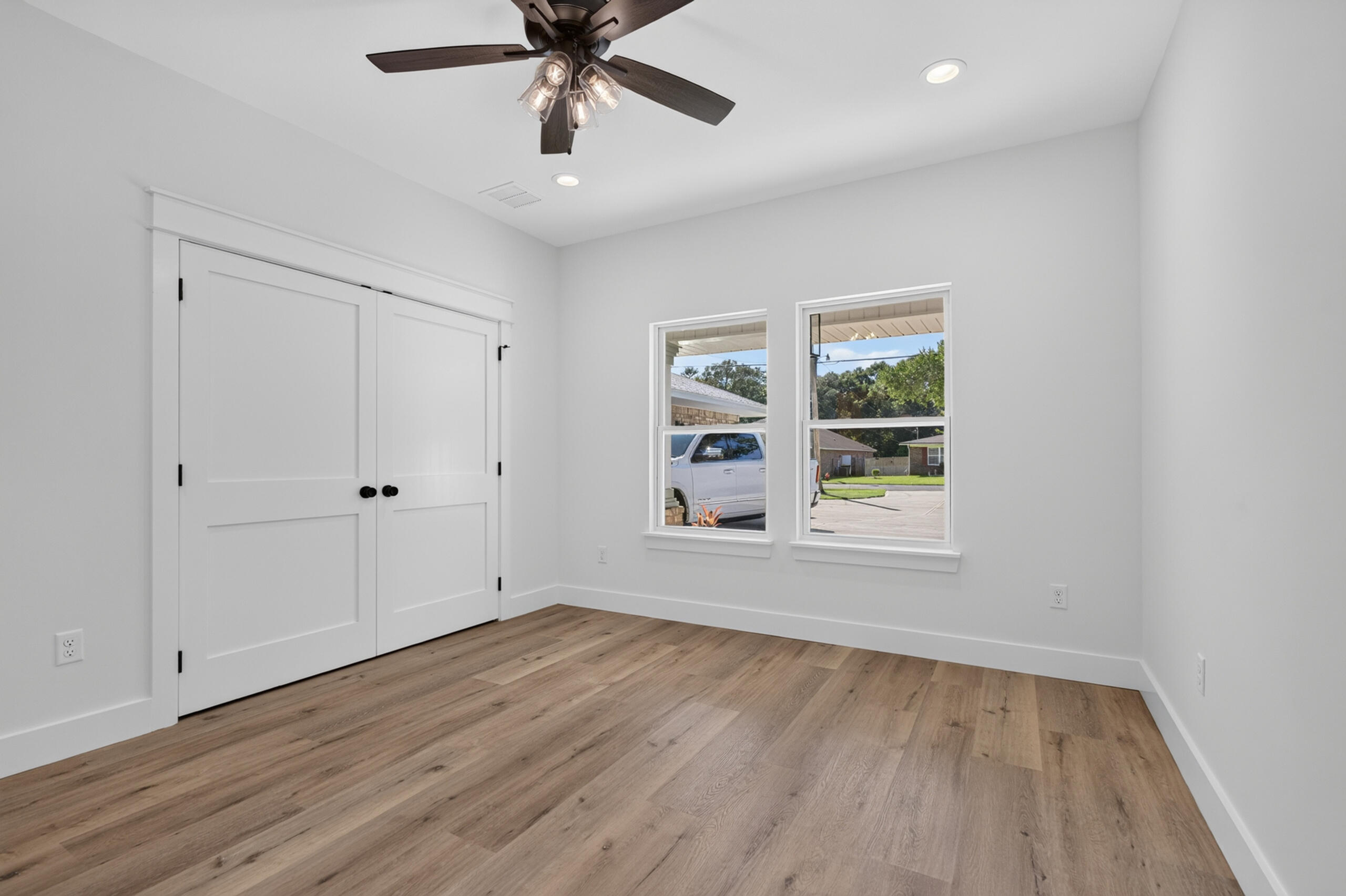 Empty room with wood flooring, double closet doors, two windows, and a ceiling fan.