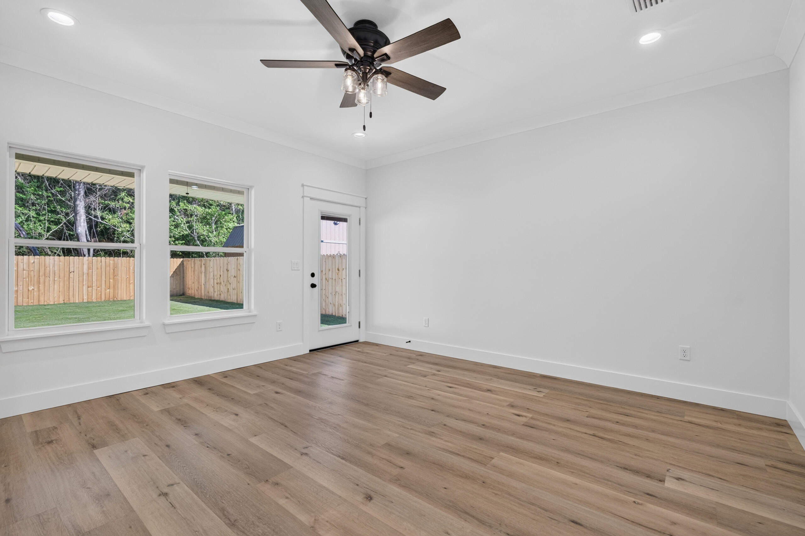 Empty room with wood-look floors, two windows, a glass-paneled door, and a ceiling fan.