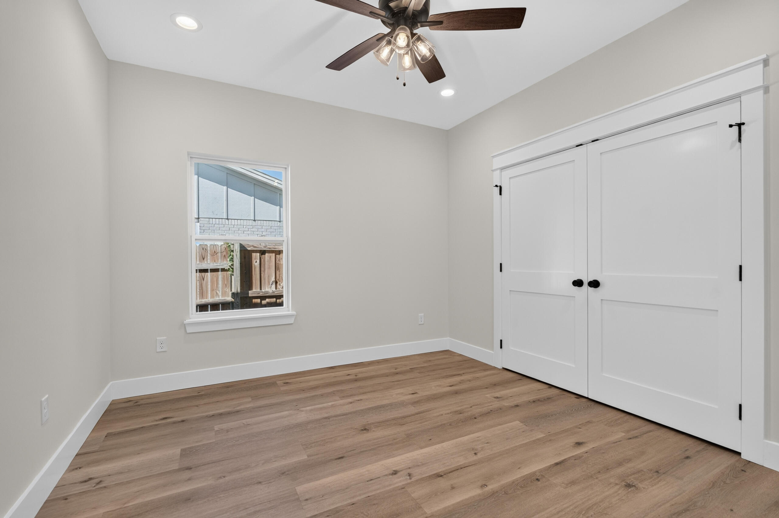 Empty bedroom with wood plank flooring, a ceiling fan, and white double closet doors.