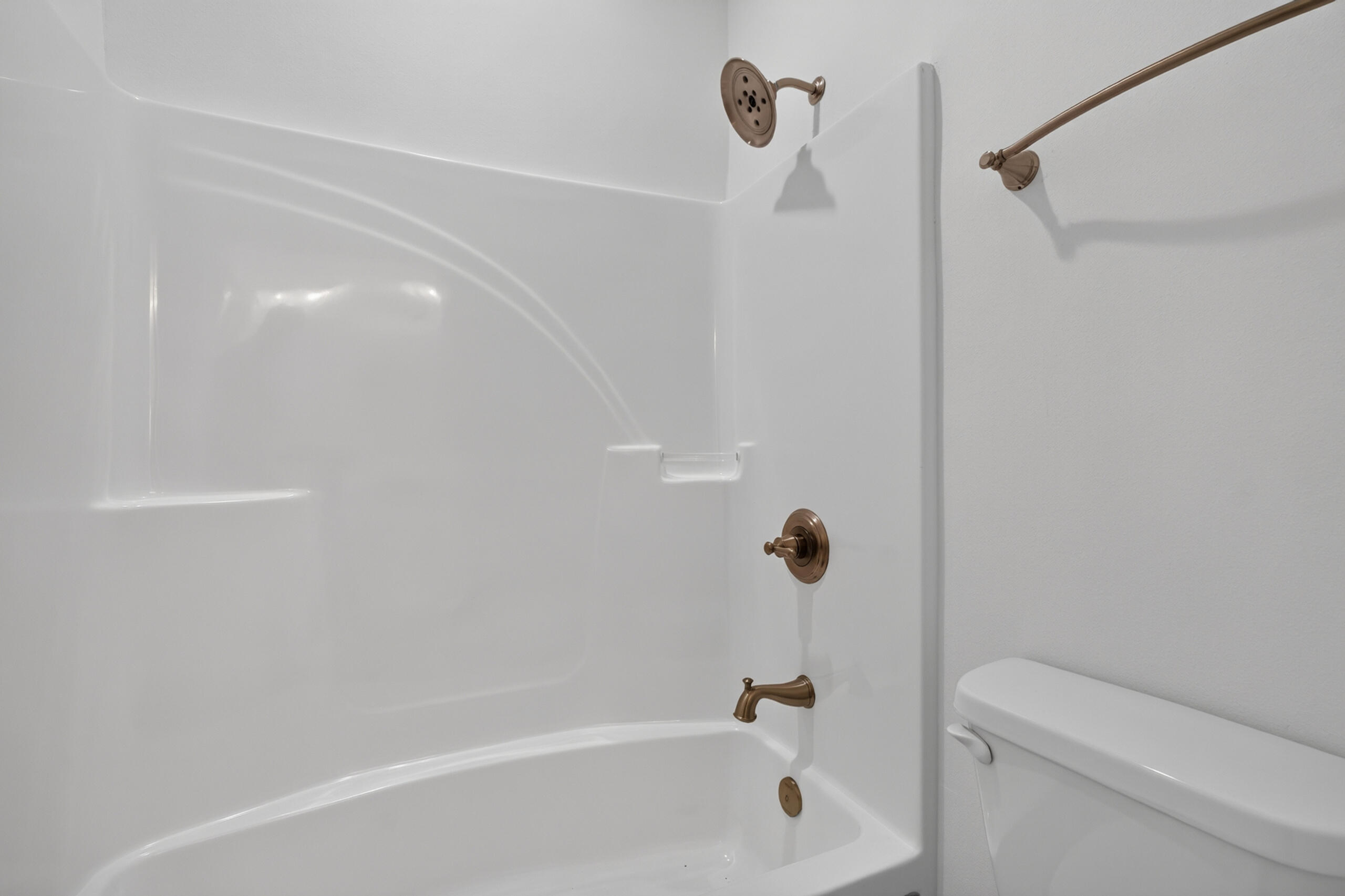 White bathtub and shower with bronze fixtures beside a toilet.