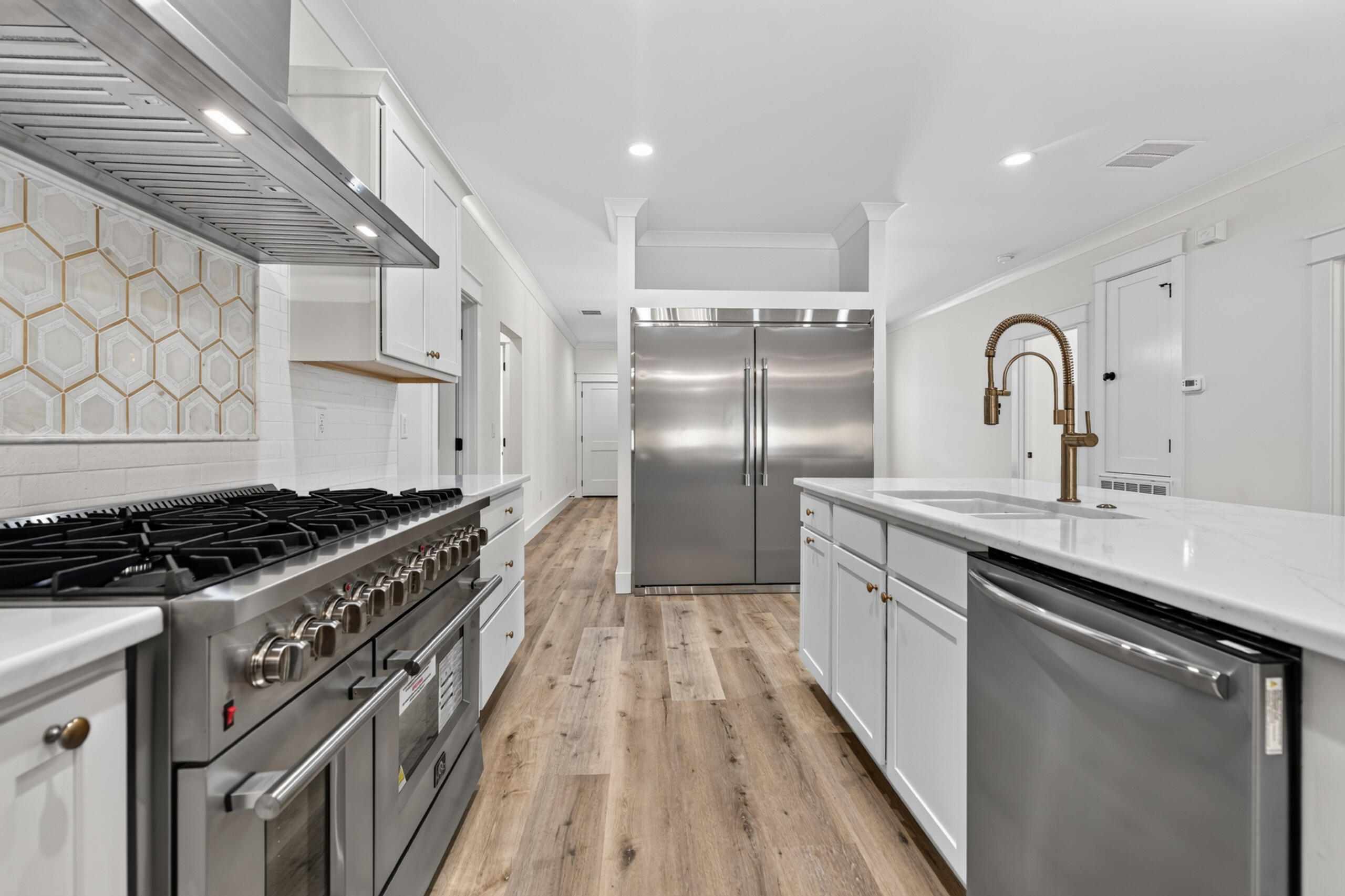 Bright white kitchen with a stainless steel range and refrigerator, patterned backsplash, and island with brass faucet.