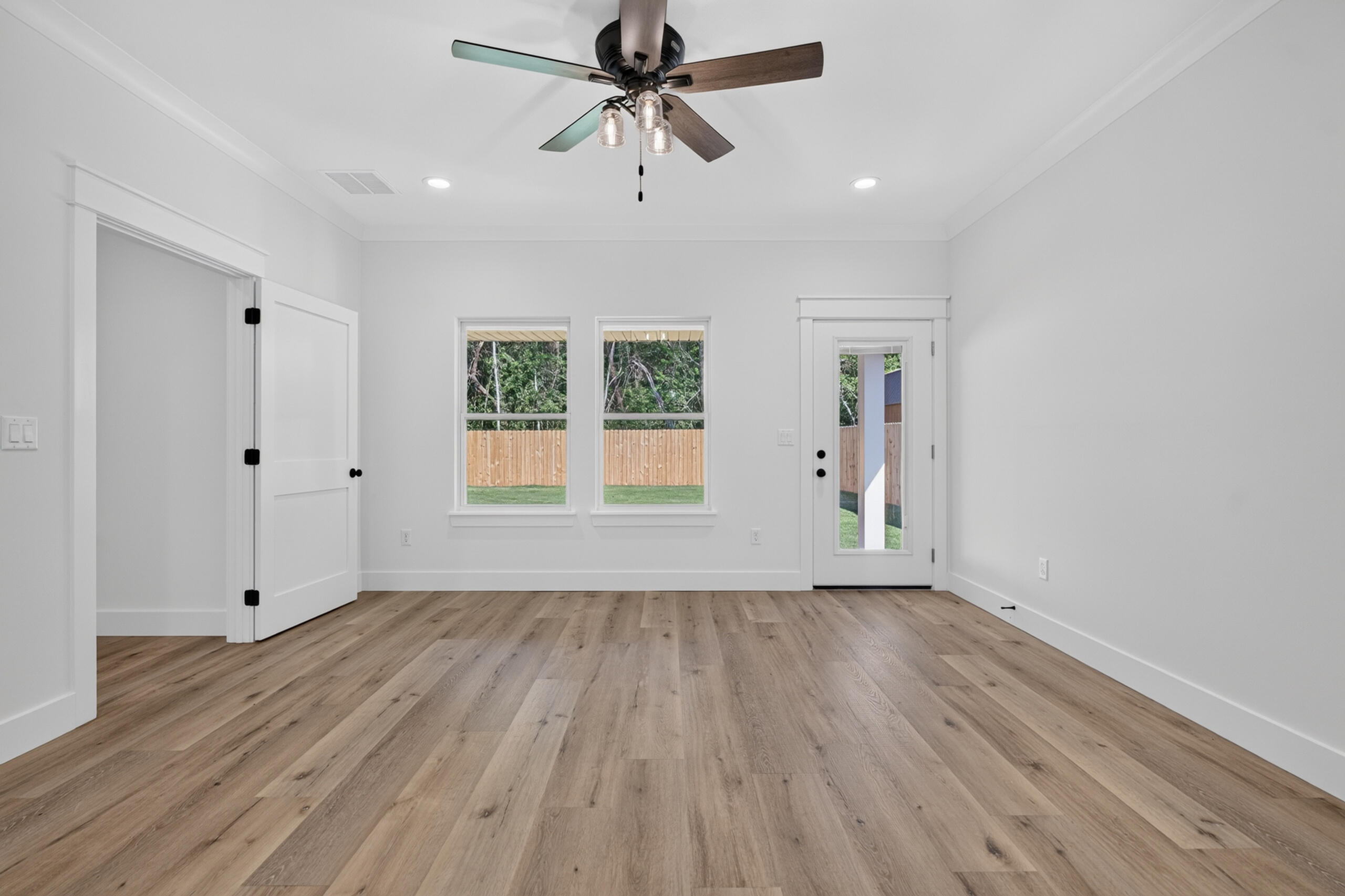 Empty room with wood-look flooring, ceiling fan, two yard-facing windows, and a glass-panel door.