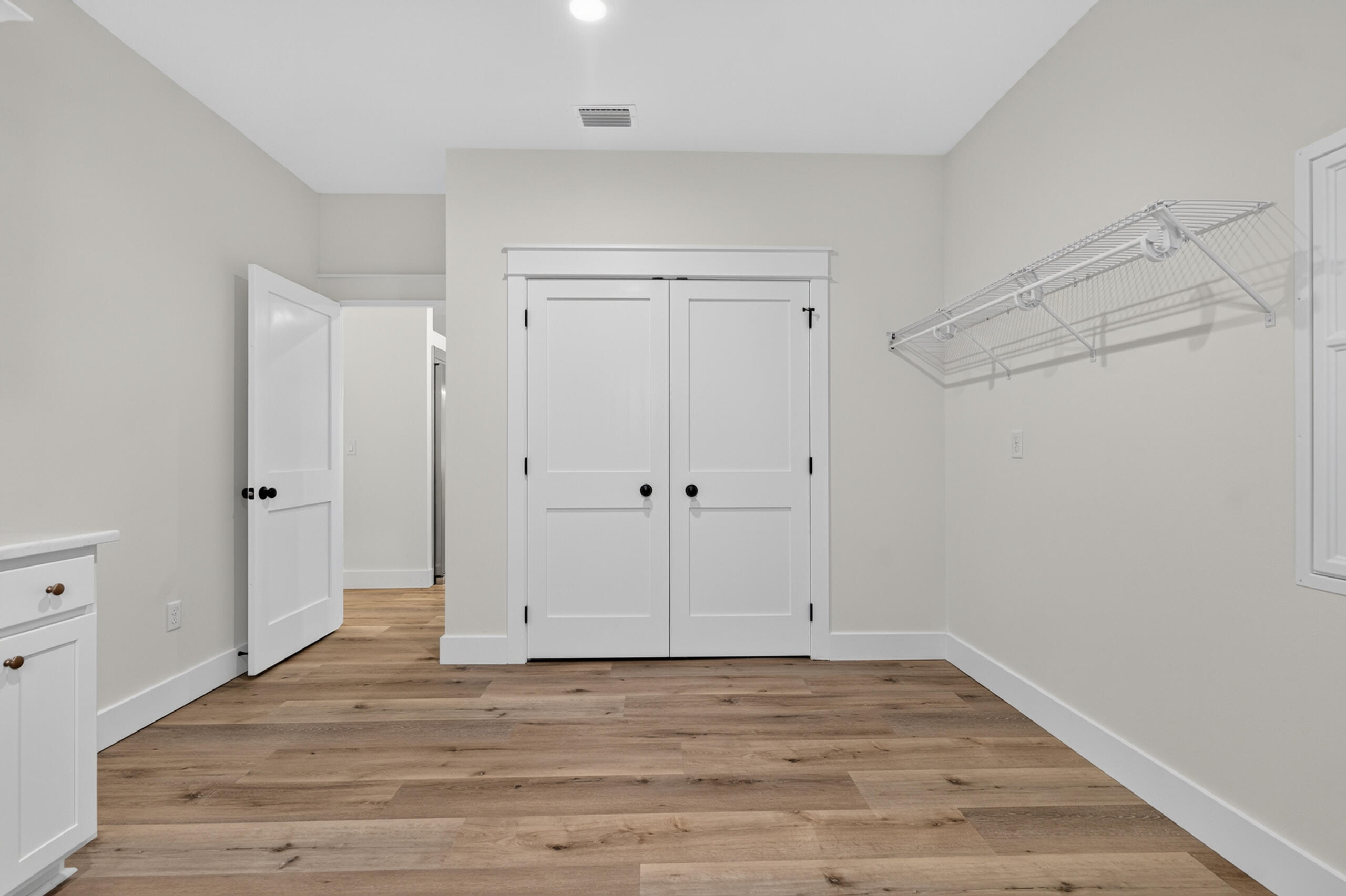Empty laundry room with a wall-mounted drying rack, white storage cabinets, and wood-look flooring.