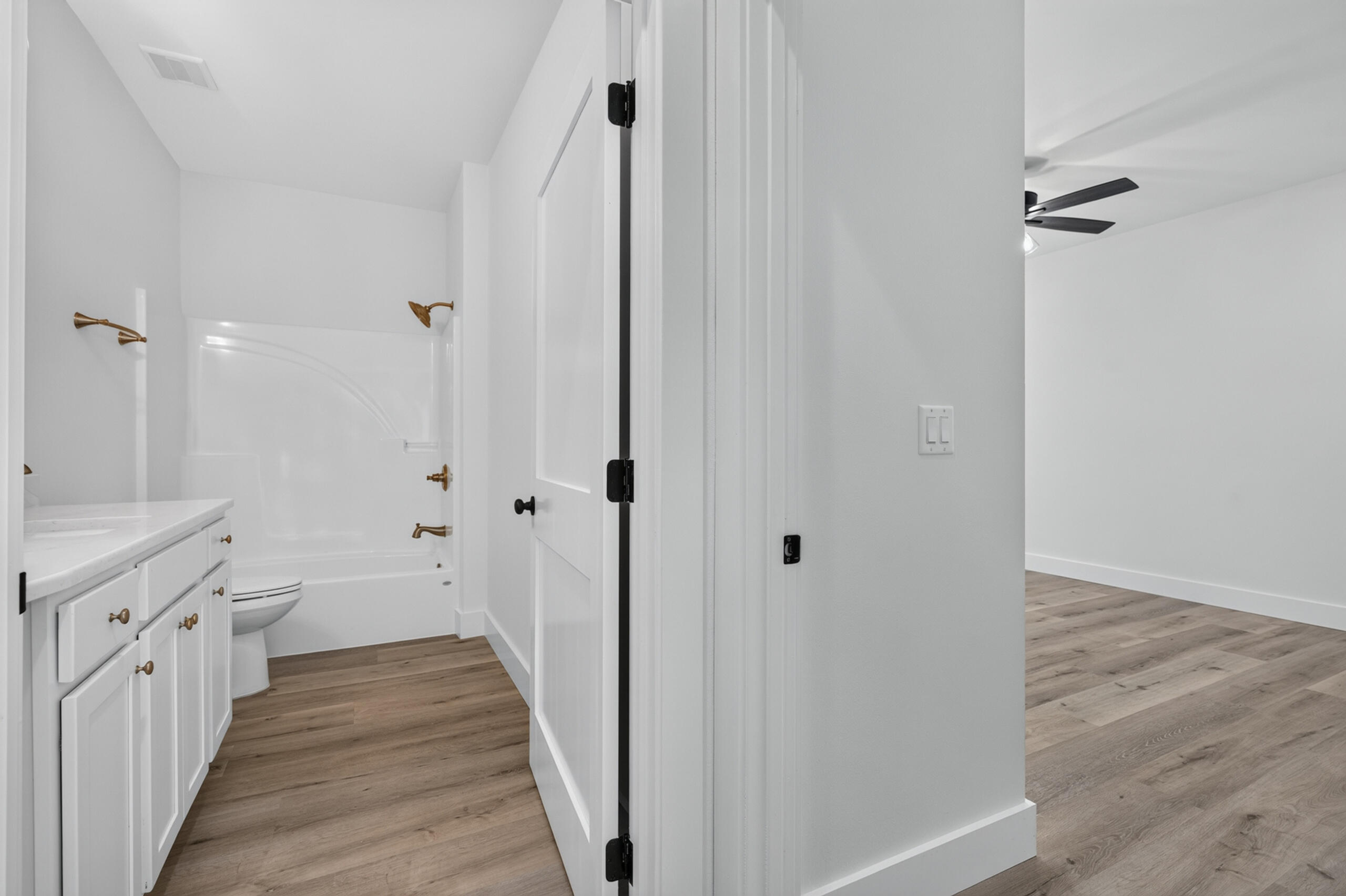 Bathroom with a white vanity and tub, opening onto an adjacent room with wood-look floors.