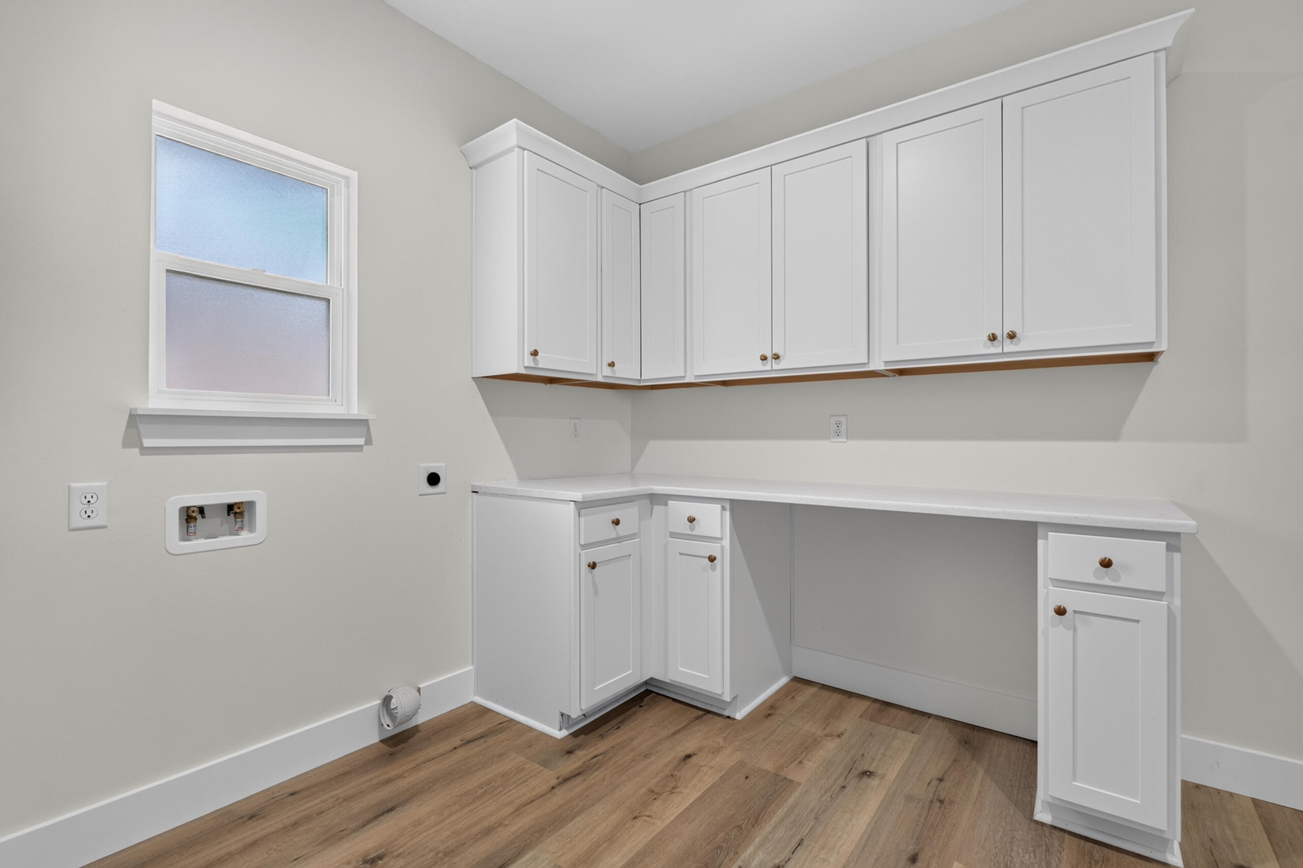 Laundry room with white cabinetry, a long counter, washer hookups, and wood-look flooring.