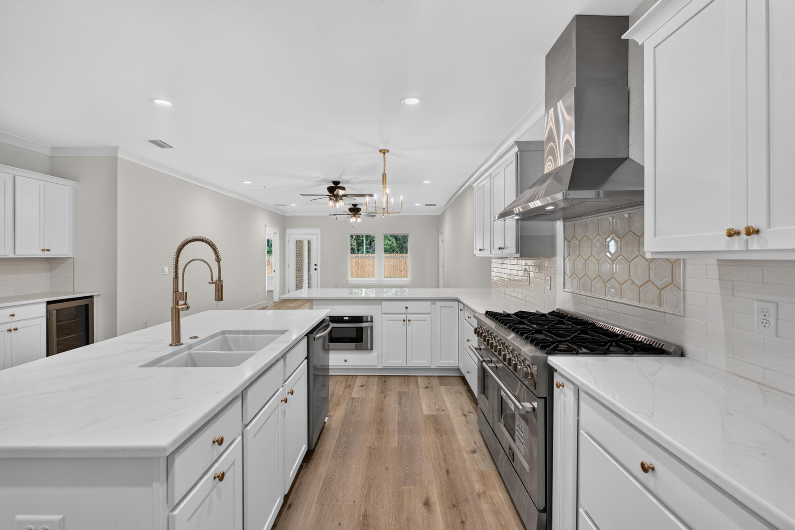 Bright white kitchen with a large island, professional range, geometric backsplash, and wood-look flooring.