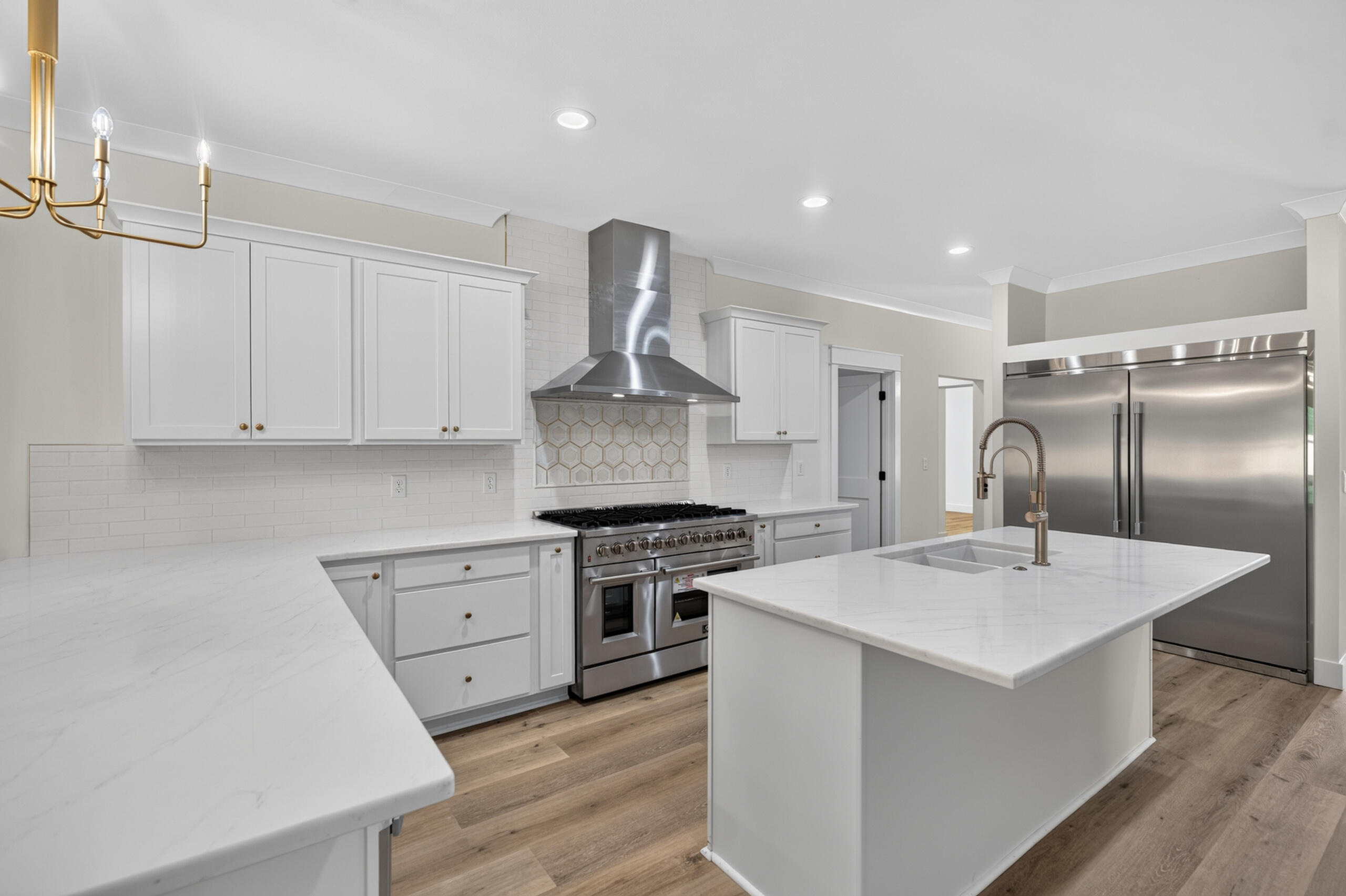 Renovated kitchen with a large white island, brass spring faucet, stainless range, and patterned backsplash.