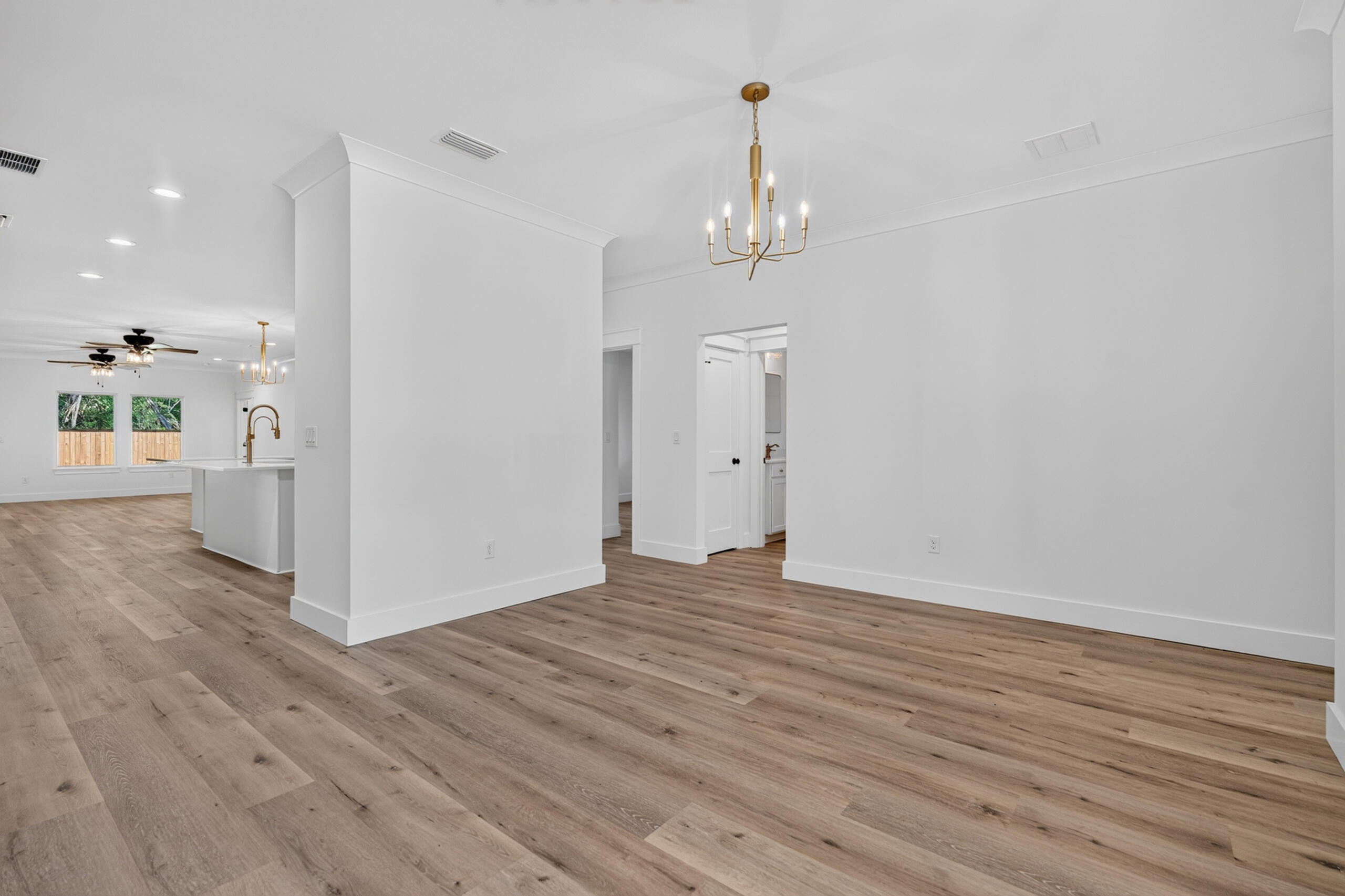 Open-plan dining area with wide-plank wood floors, brass chandelier, and kitchen island.