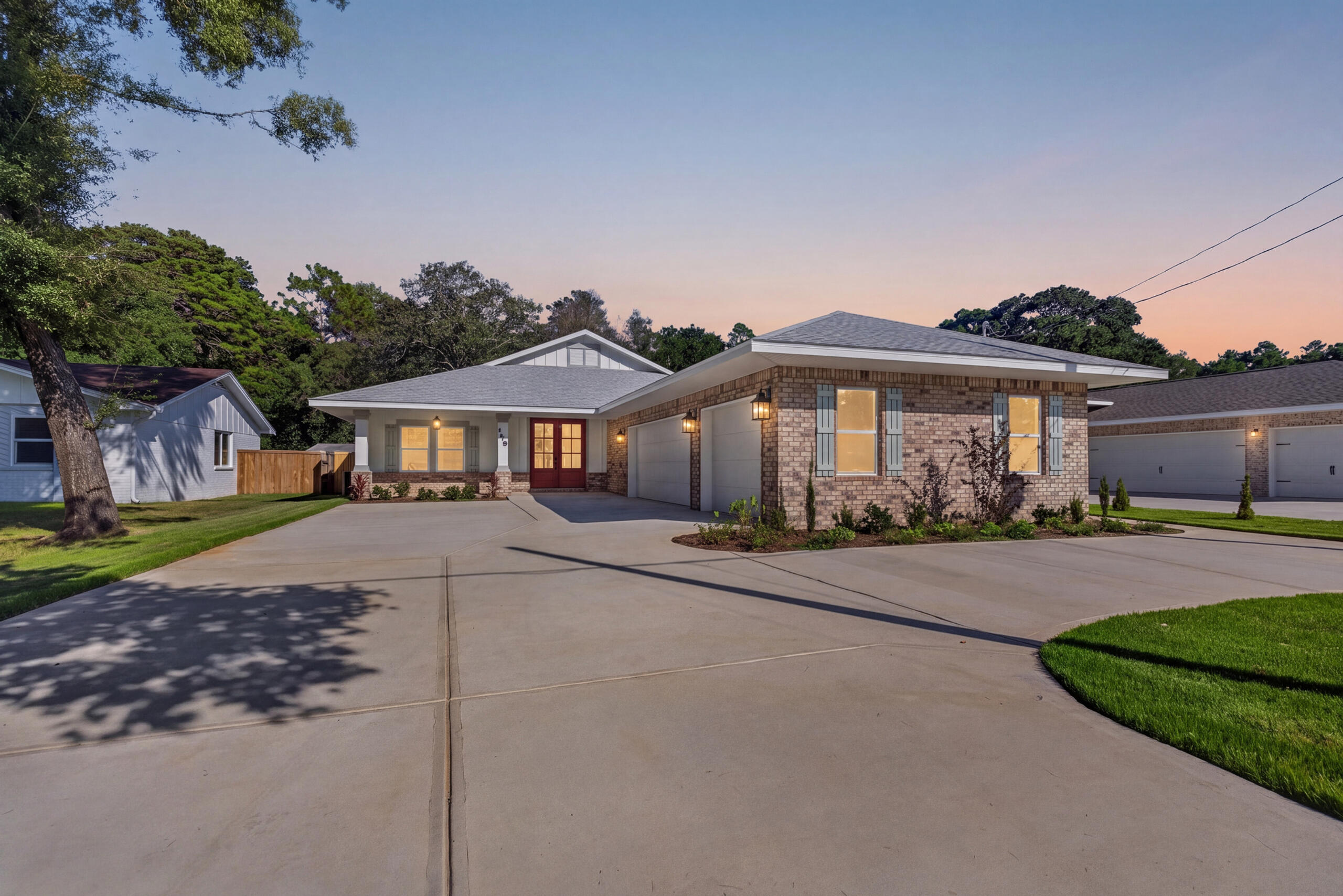 Brick single-story home with red front door, attached garage, and broad driveway at dusk.