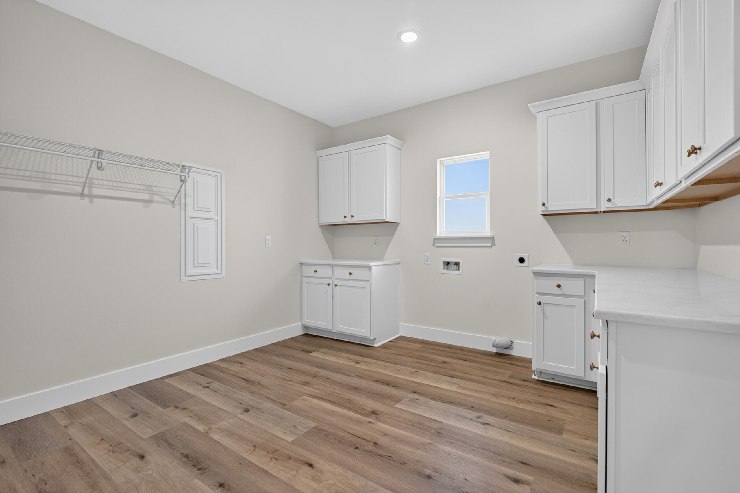 Empty laundry room with white cabinets, washer hookups, wire shelving, and wood-look plank flooring.