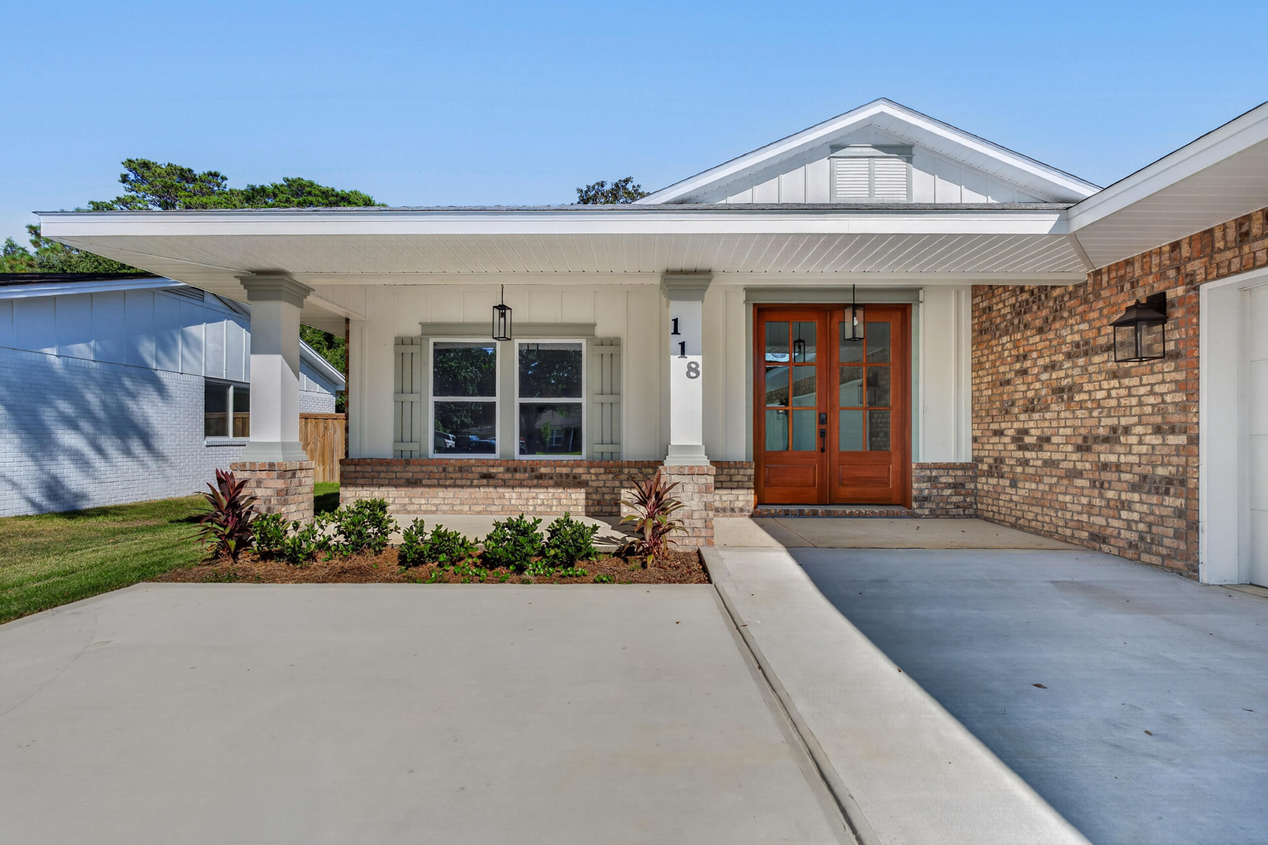 Home exterior with a broad covered porch, brick walls, and wooden double entry doors.