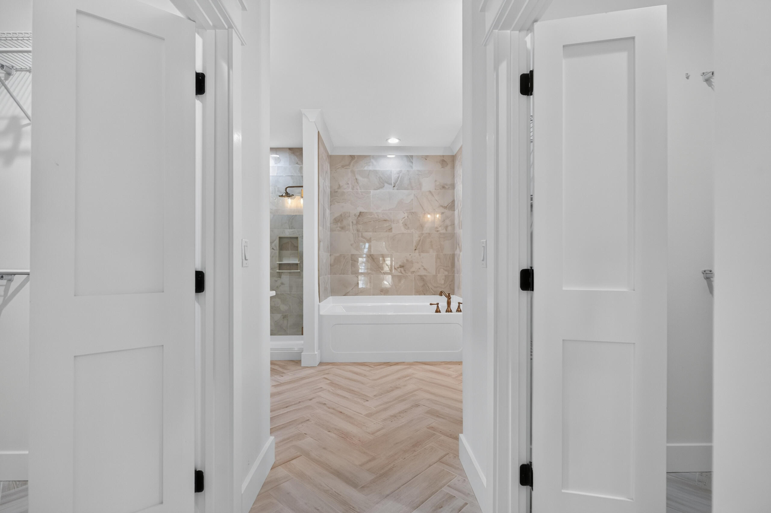 Bathroom with a white tub, beige tiled surround, bronze fixtures, and herringbone wood-look flooring.