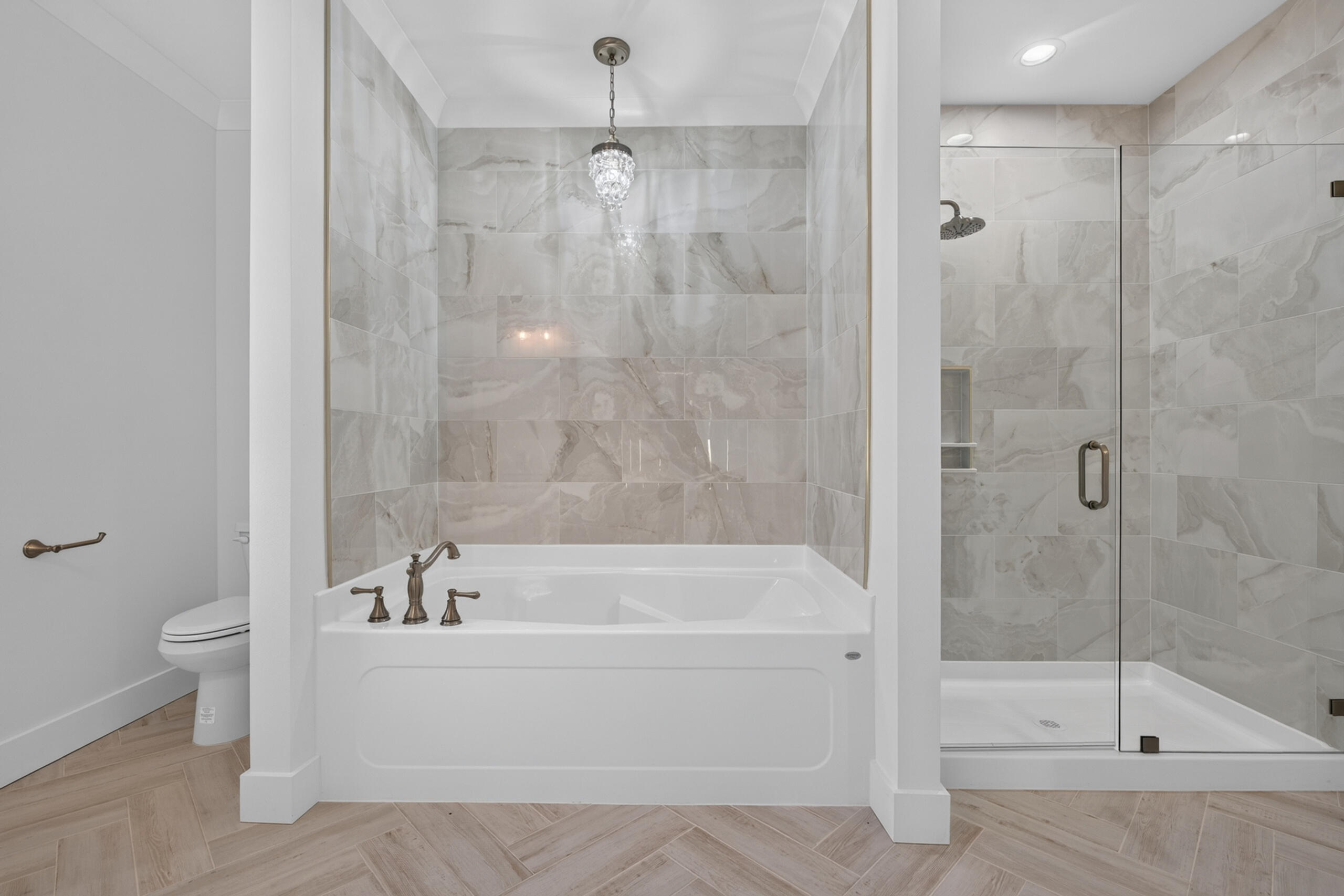 Bathroom with a soaking tub, crystal pendant light, marble-look tile, and glass-enclosed shower.