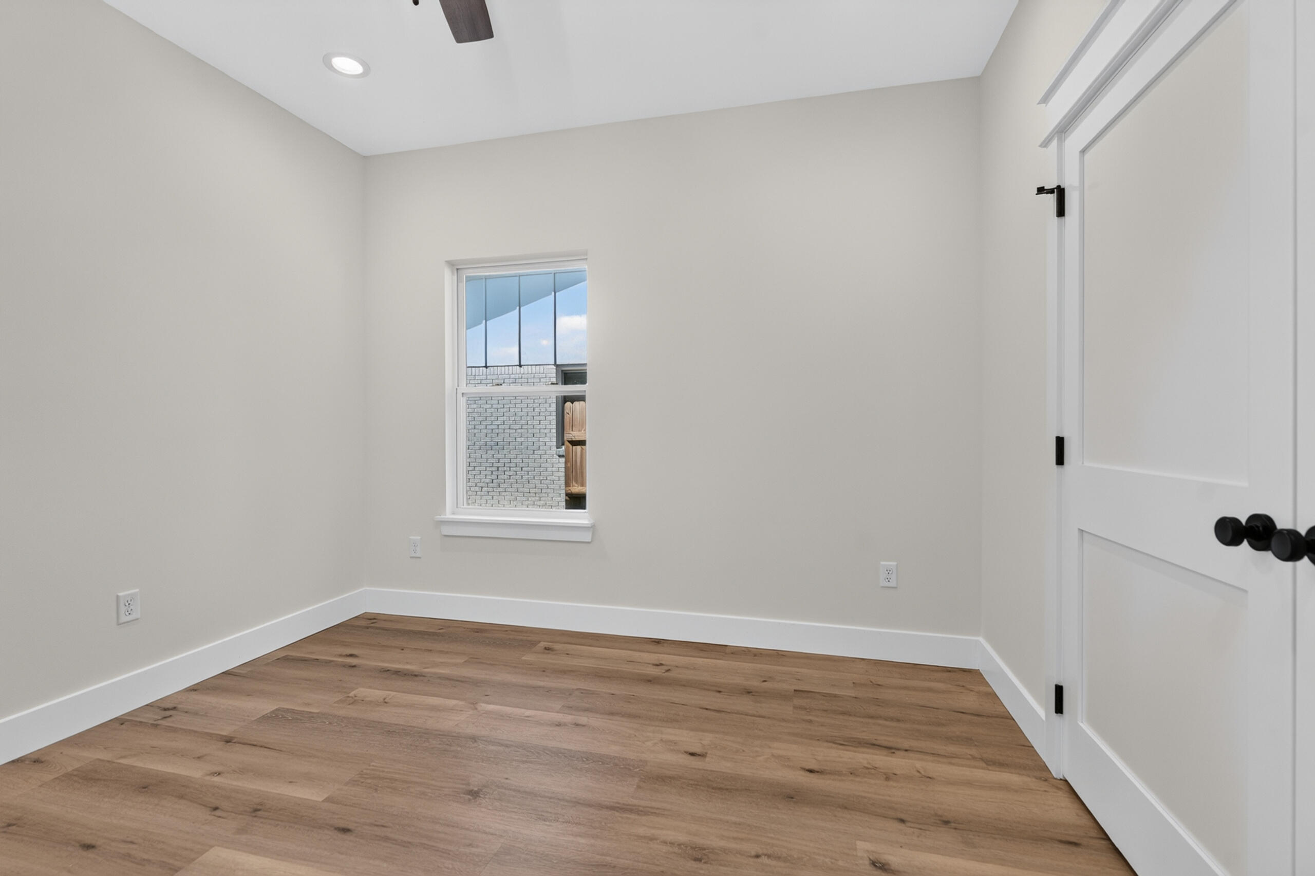Empty room with wood plank flooring, a window, and white double doors.