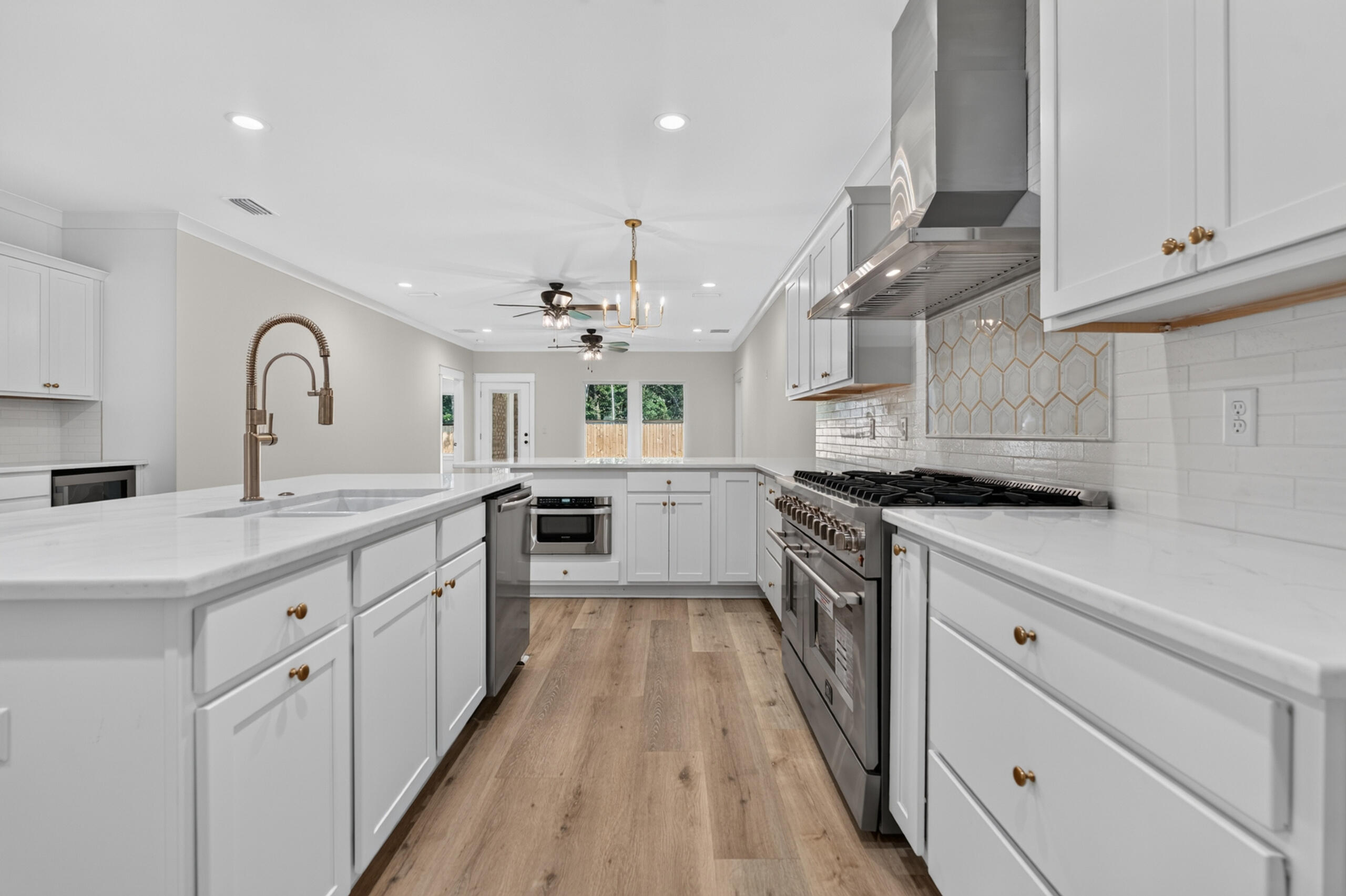 Bright white kitchen with a large island, brass faucet, stainless steel range, and geometric tile accent.