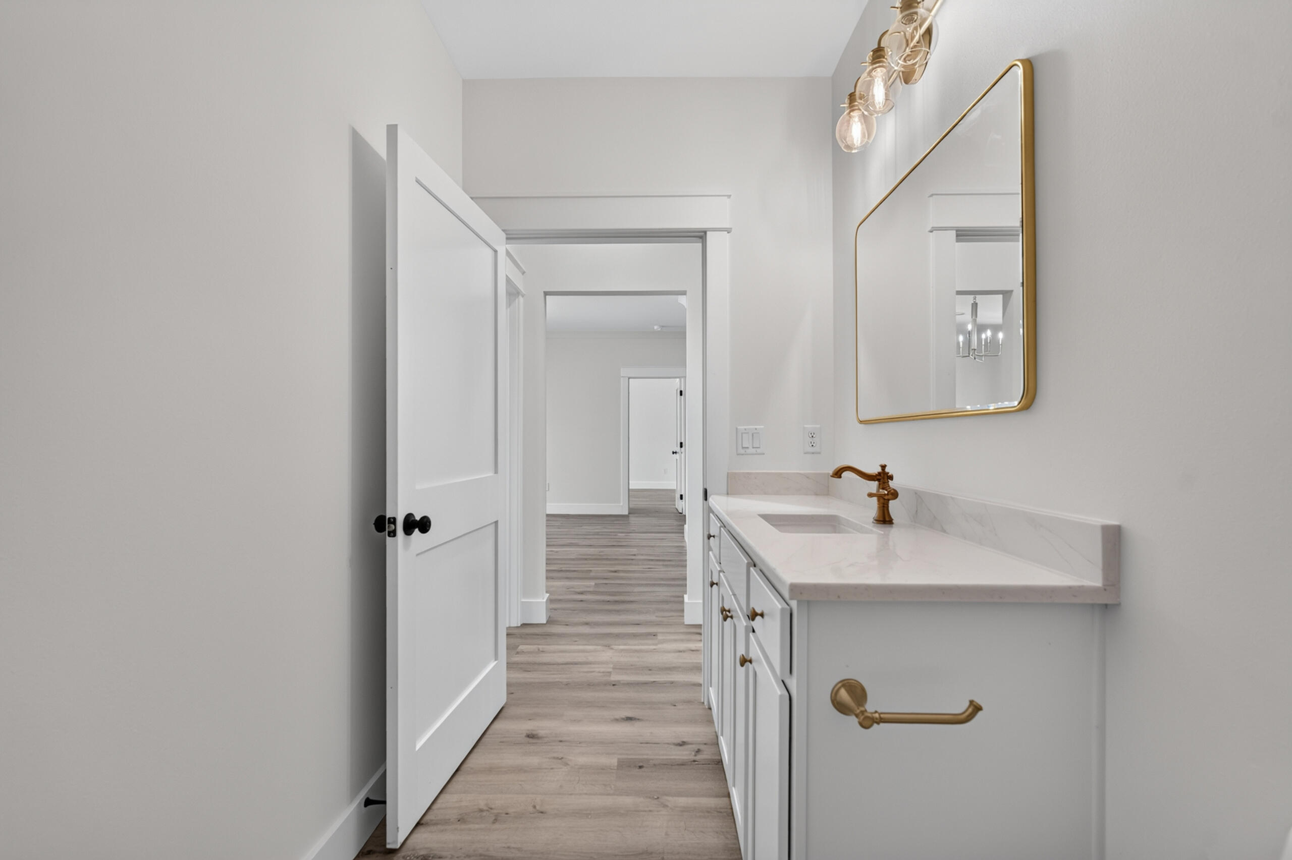 Bathroom vanity with brass fixtures and a gold-framed mirror beside an open hallway door.
