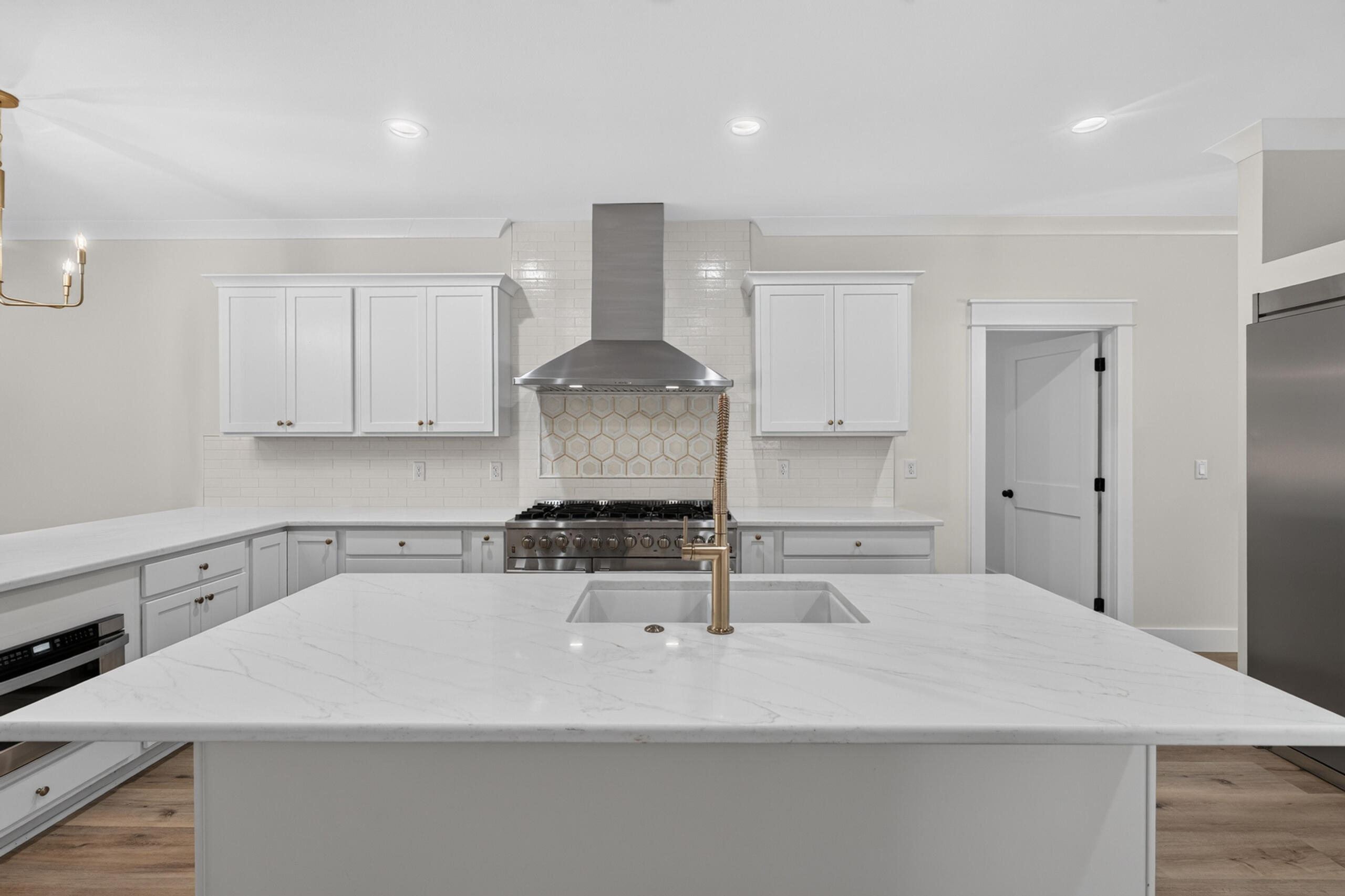 Bright white kitchen with a large marble-look island, brass faucet, and stainless steel range.
