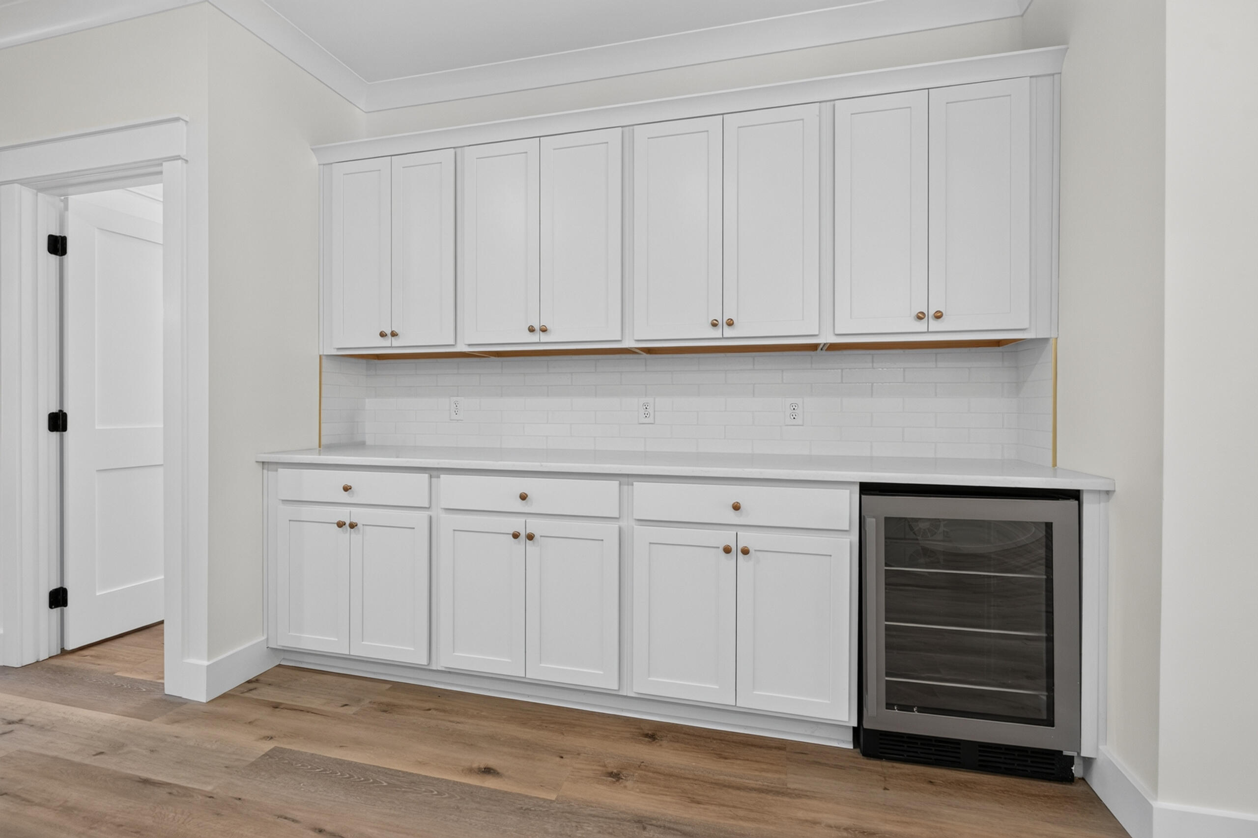 Kitchen with white shaker cabinets, subway-tile backsplash, and a glass-front beverage refrigerator.