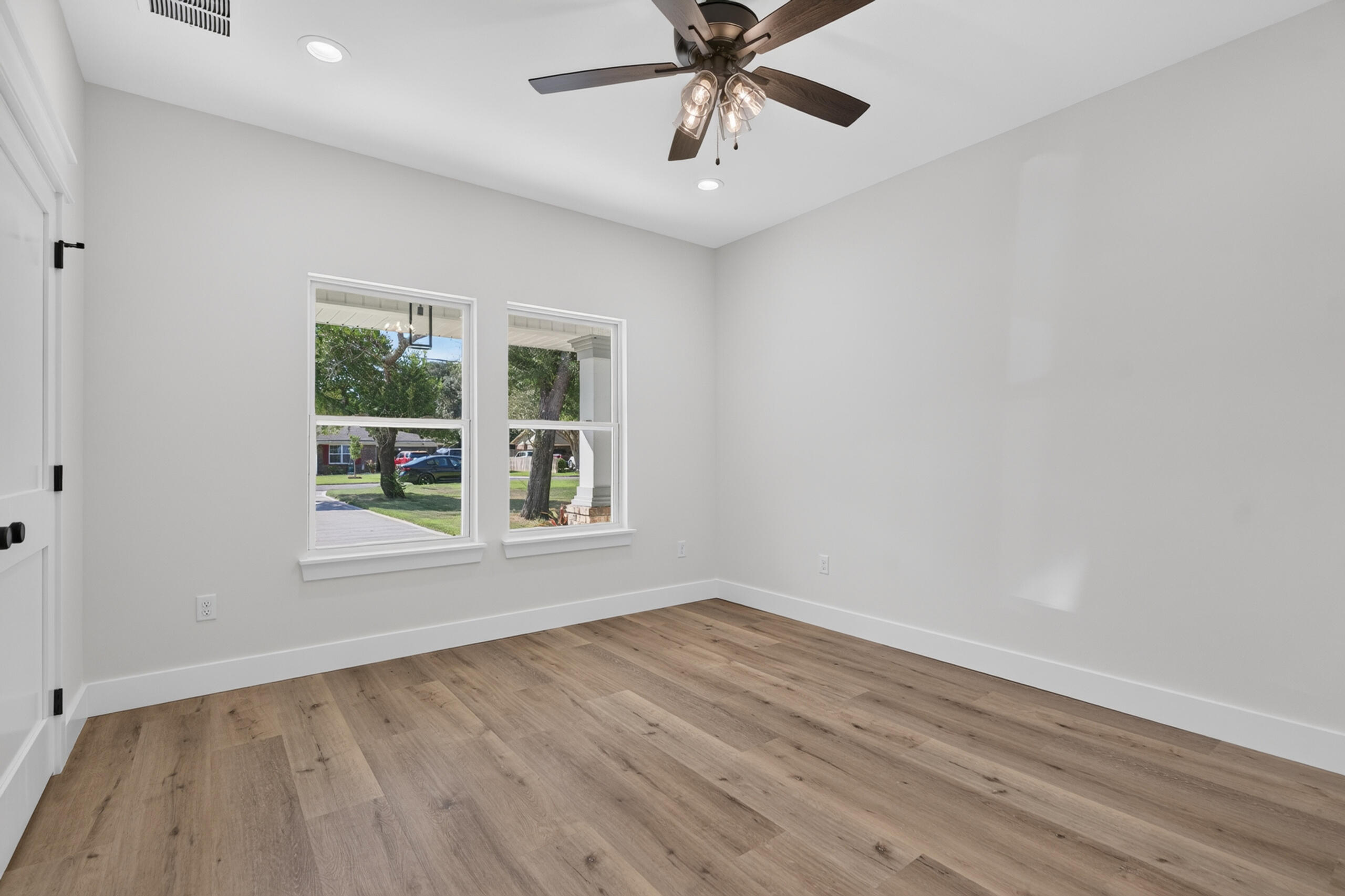 Empty room with wide-plank wood-look floors, two windows, and a ceiling fan.