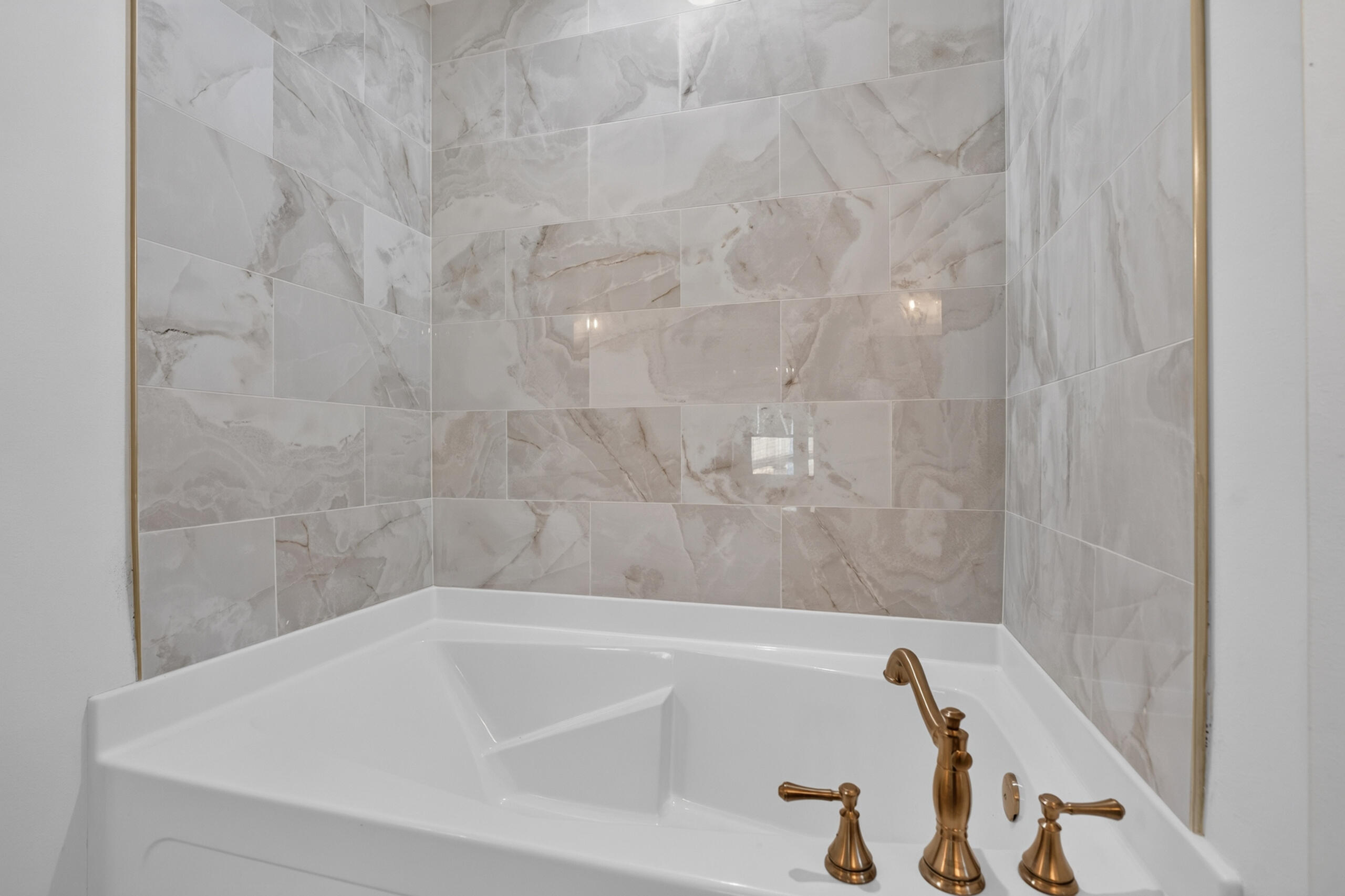 Corner bathtub with marble-pattern tile walls and bronze faucet fixtures.