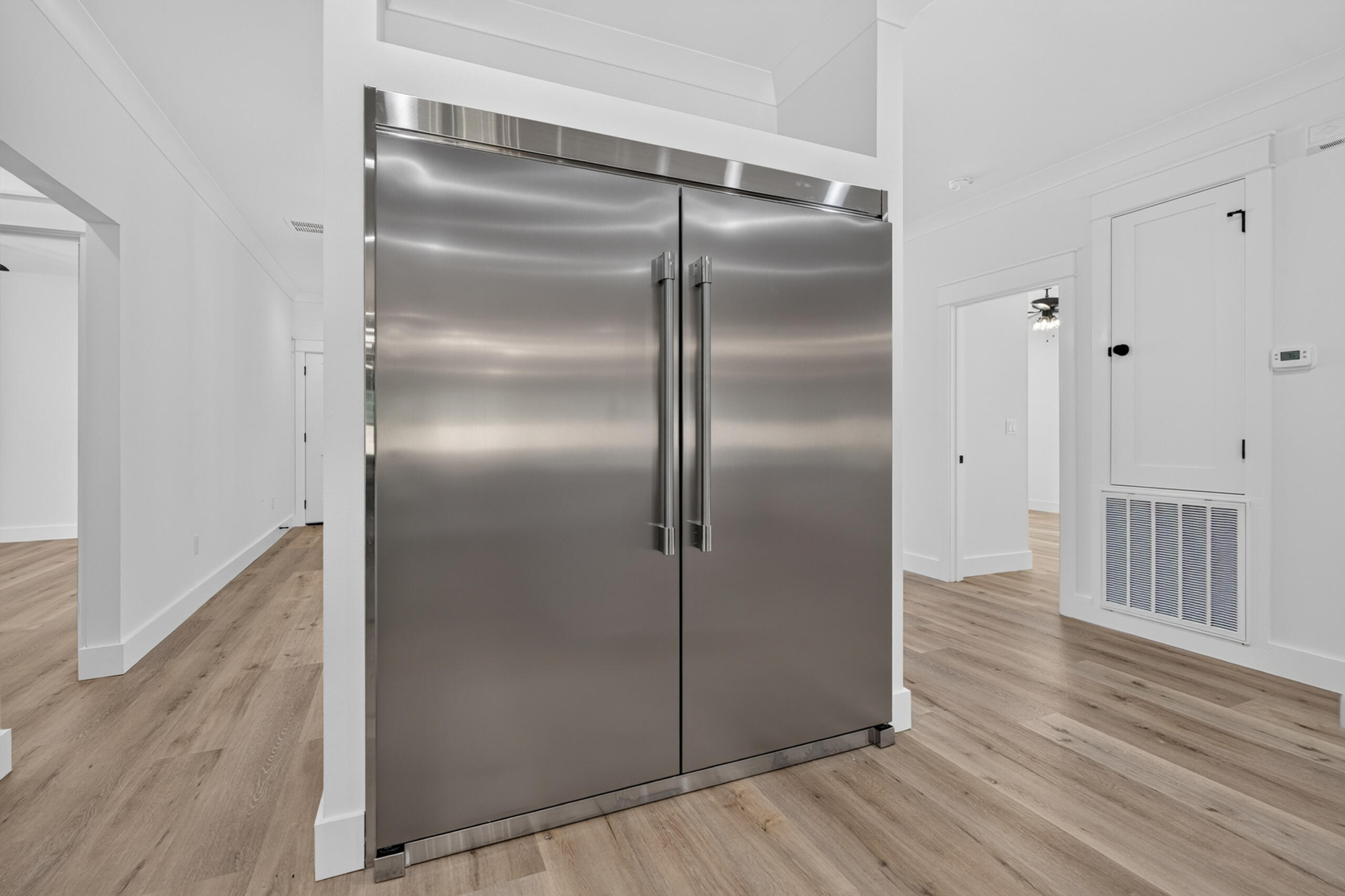 Stainless steel side-by-side refrigerator in a bright interior with light wood-look flooring.