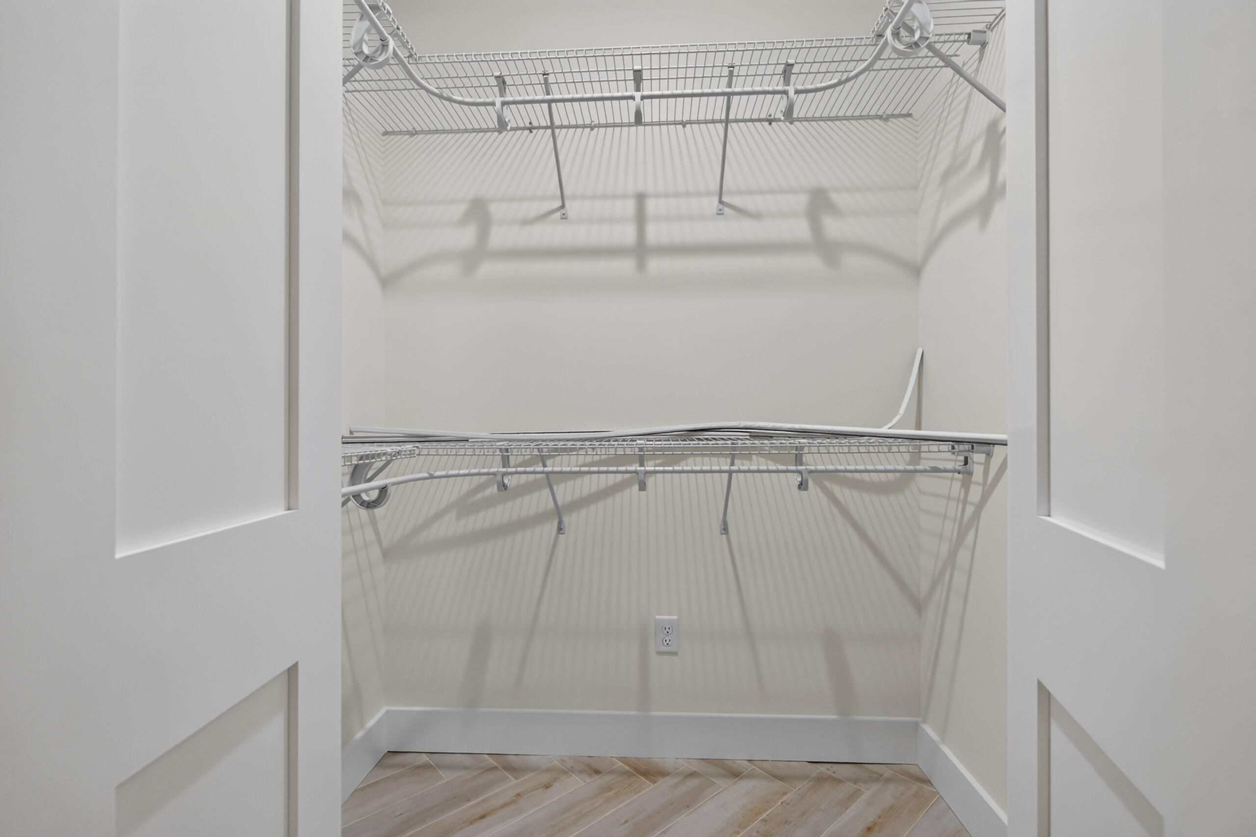 Walk-in closet with two levels of wire shelving and a wood-look tile floor.