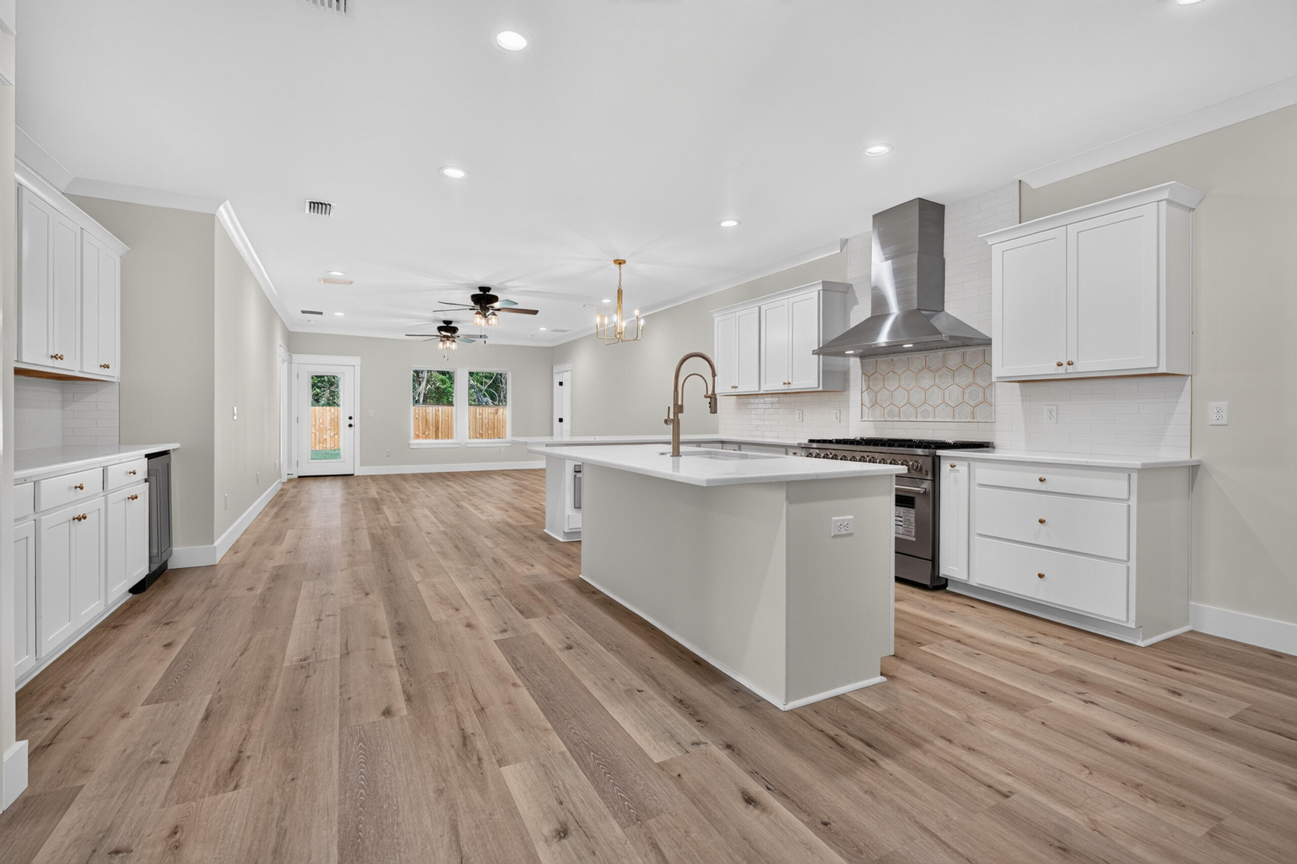 Open-plan kitchen with white cabinets, a large island, stainless steel range hood, and wood-look flooring.