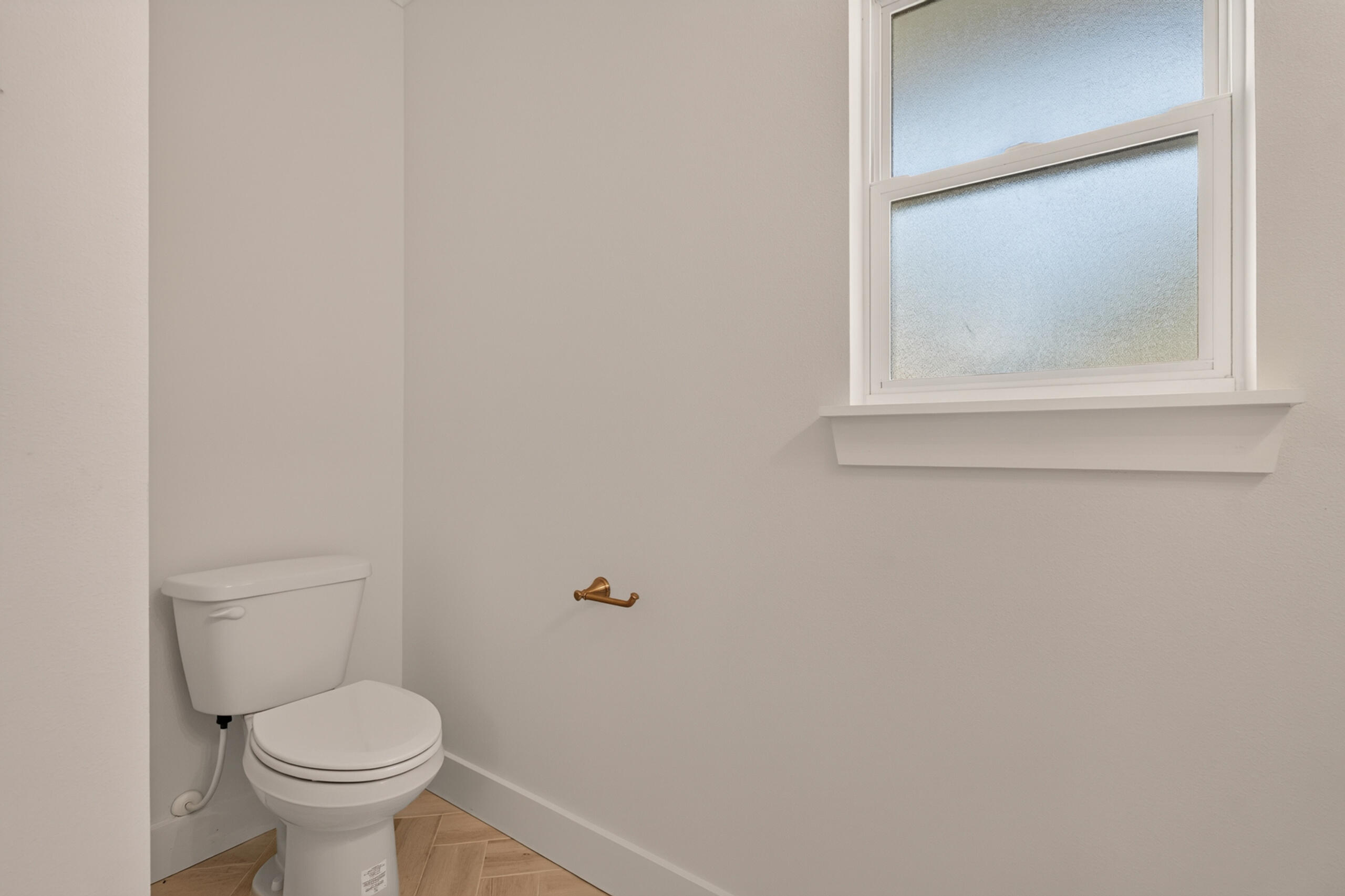 Bathroom with a white toilet, brass holder, frosted window, and herringbone tile floor.