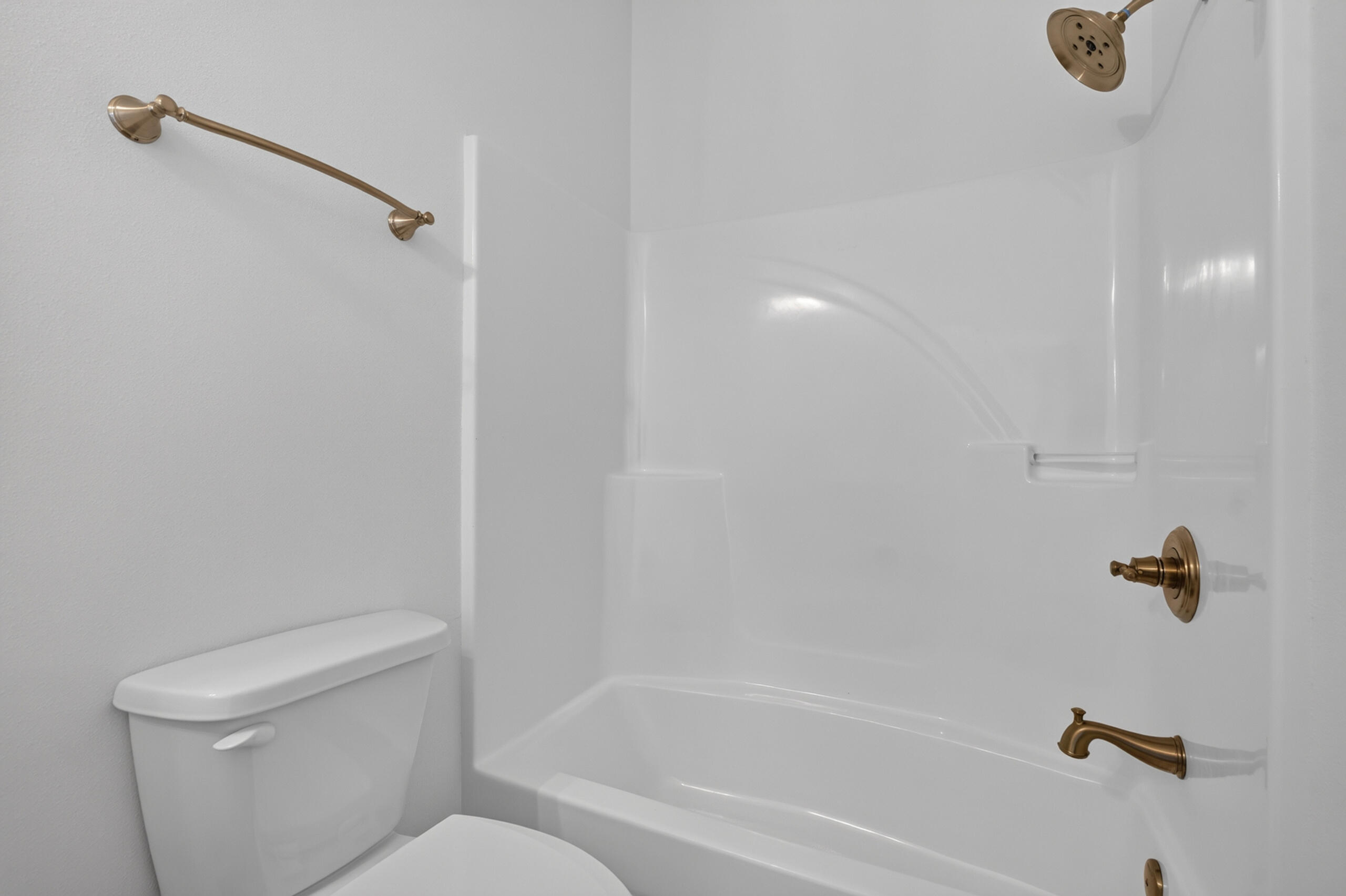 Bathroom with a white tub-shower, toilet, and bronze-colored fixtures.