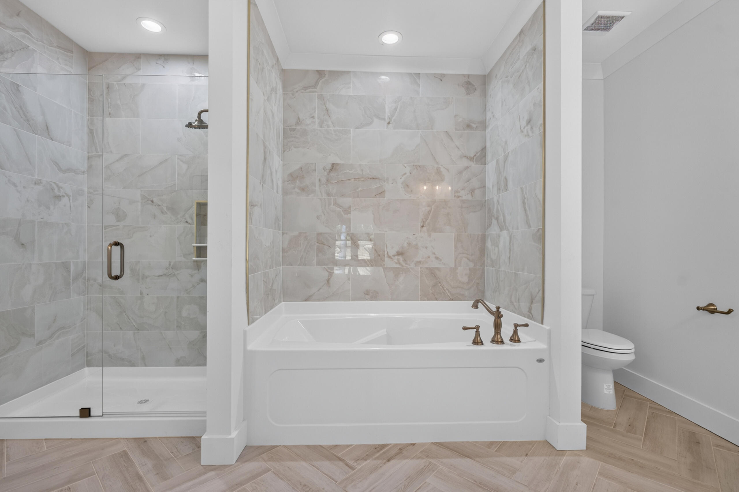 Bathroom with a soaking tub, glass-enclosed shower, marble-look tile, and bronze fixtures.