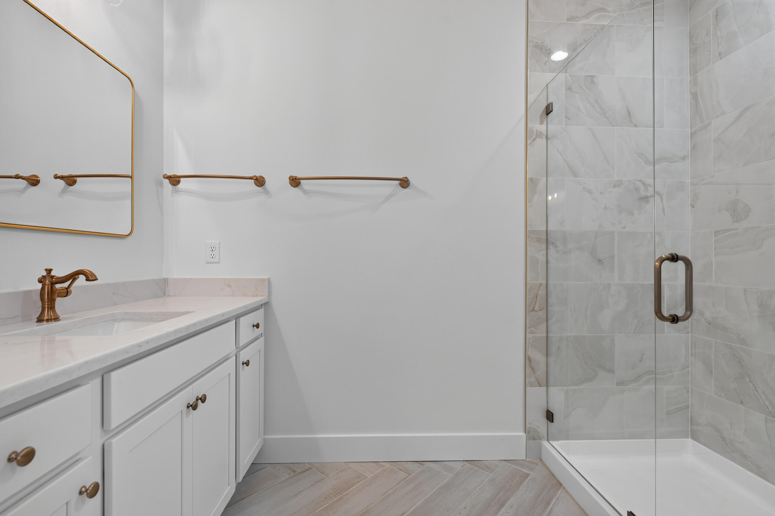 Bathroom with a white vanity and brass fixtures beside a glass-enclosed marble-look tile shower.