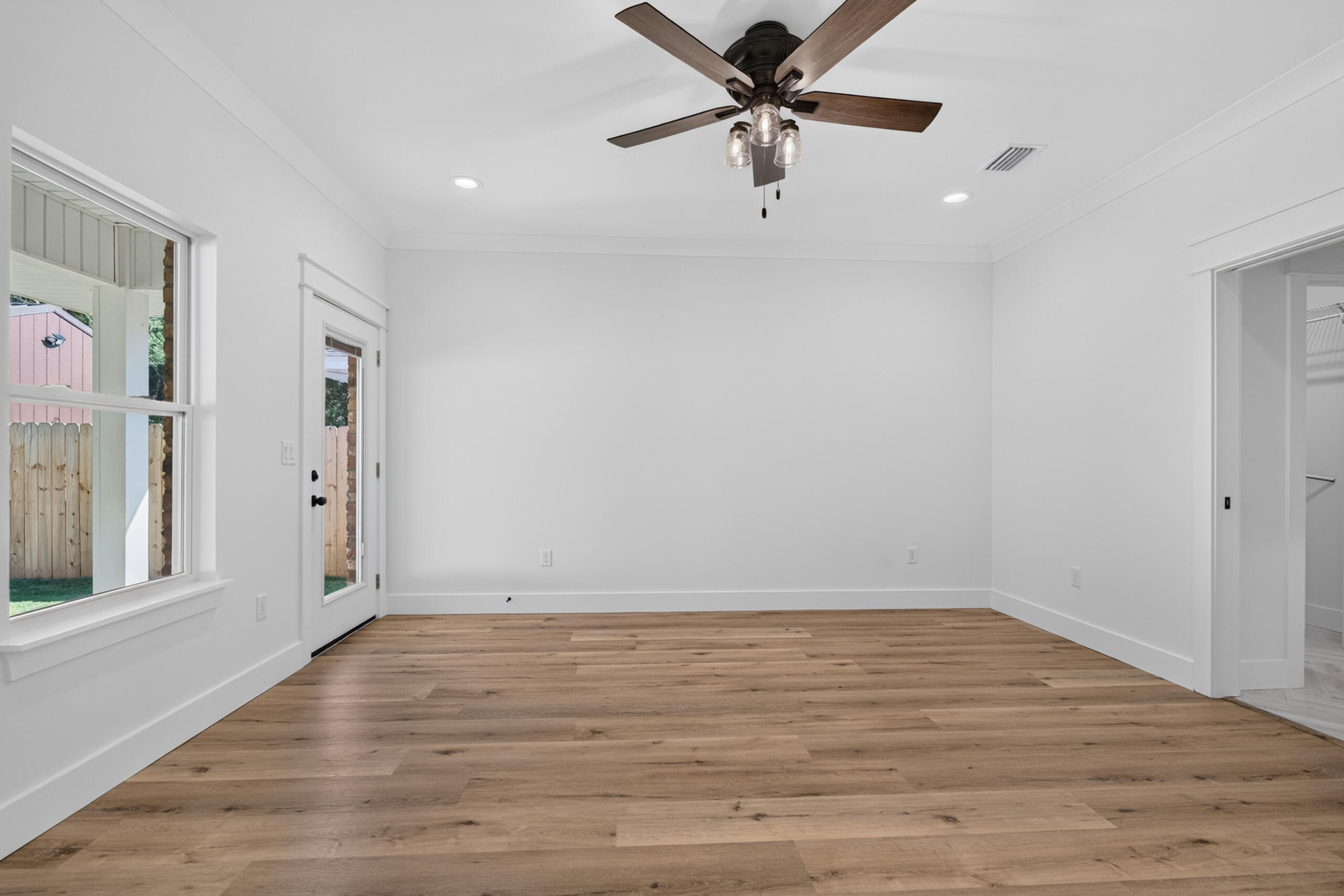 Empty room with wood flooring, a ceiling fan, a window, and a glass exterior door.